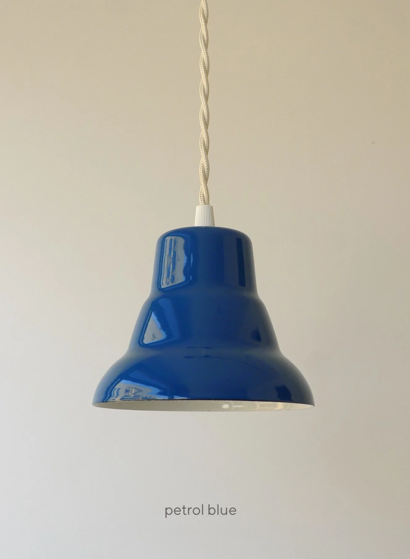 A petrol blue pendant light fixture with a white braided cord. The glossy, bell-shaped shade is a deep blue color.
