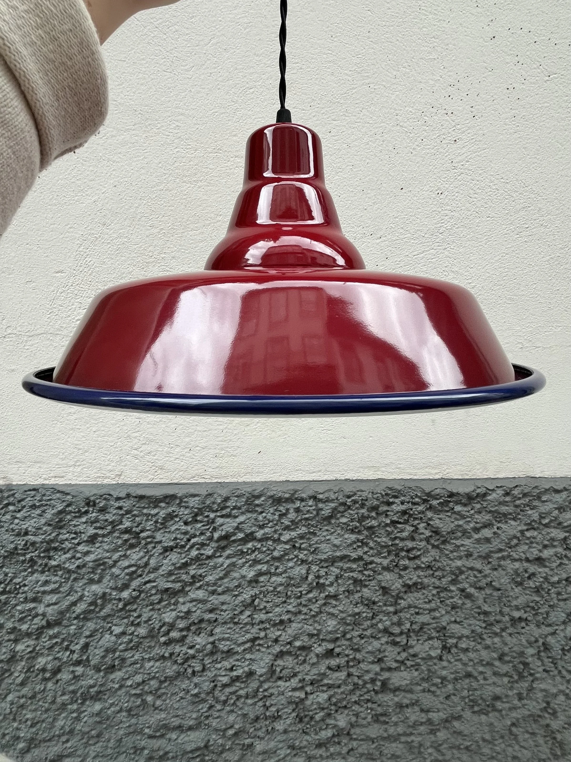 Burgundy hanging lamp with a black twist cord, viewed from below against a plain white ceiling and gray textured wall.