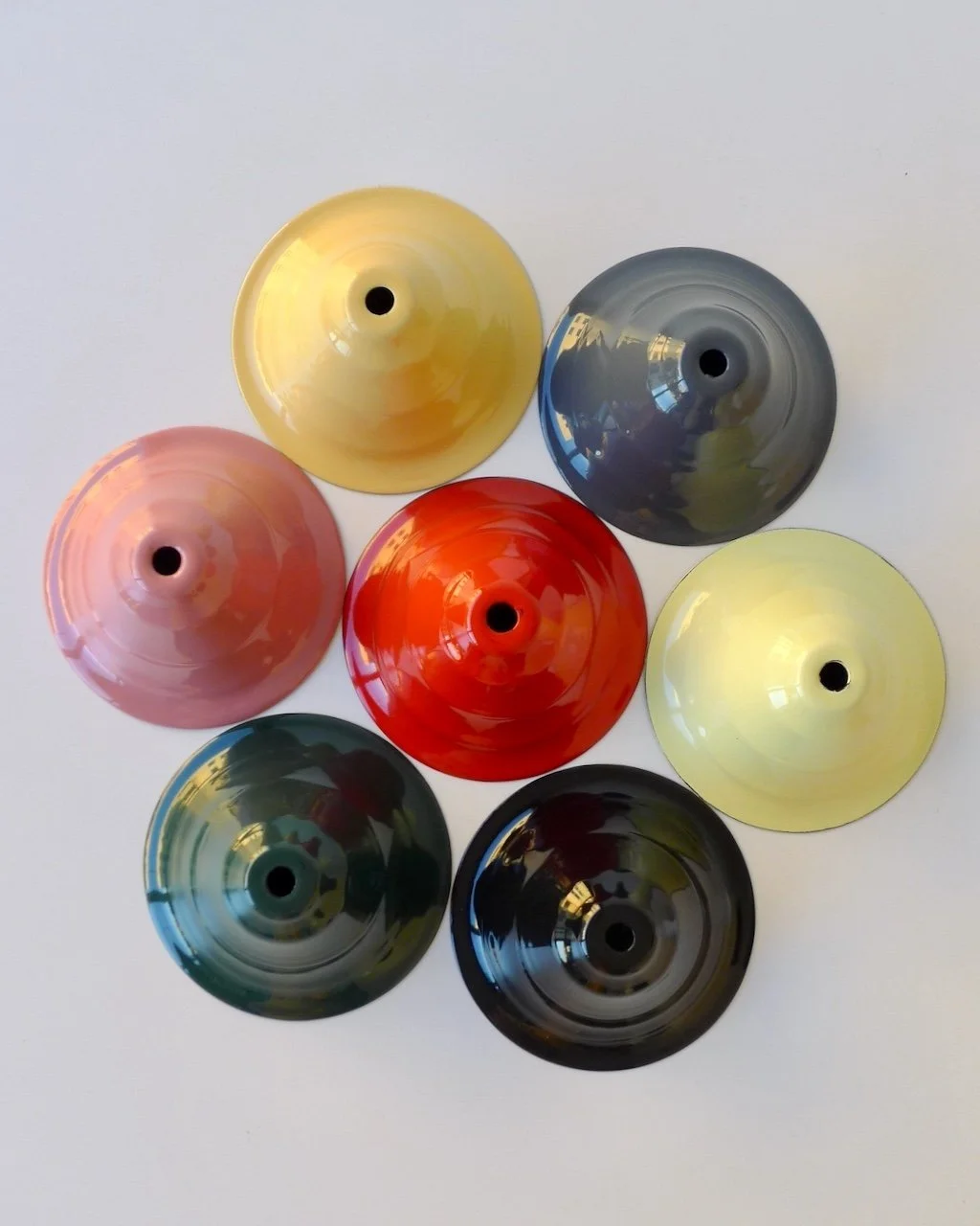 Top view of seven colorful ceiling roses bowls arranged in a circular pattern on a white surface.