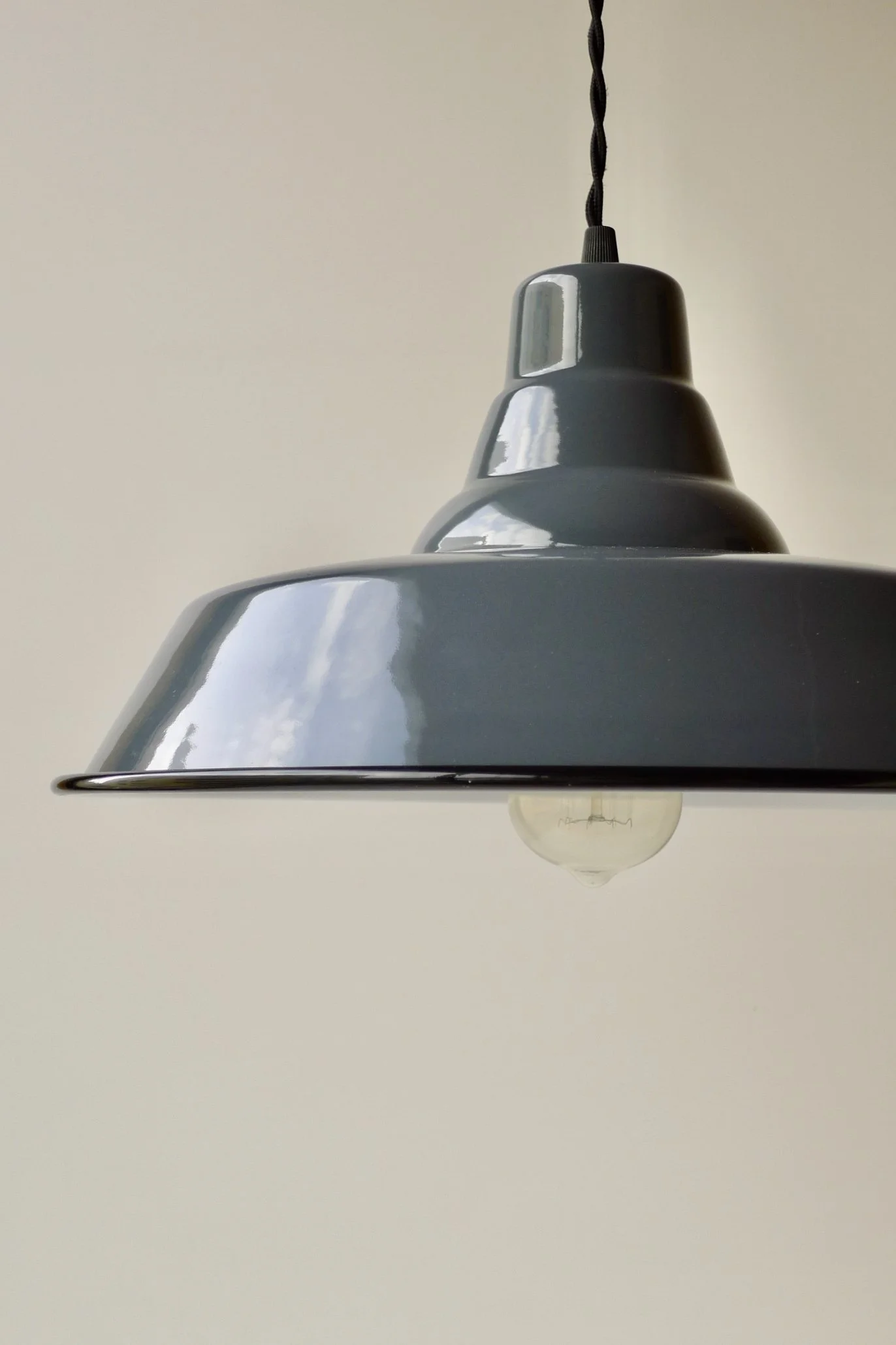 Close-up of a dark-grey pendant light fixture with a black cord and an exposed bulb hanging underneath, against a light background.