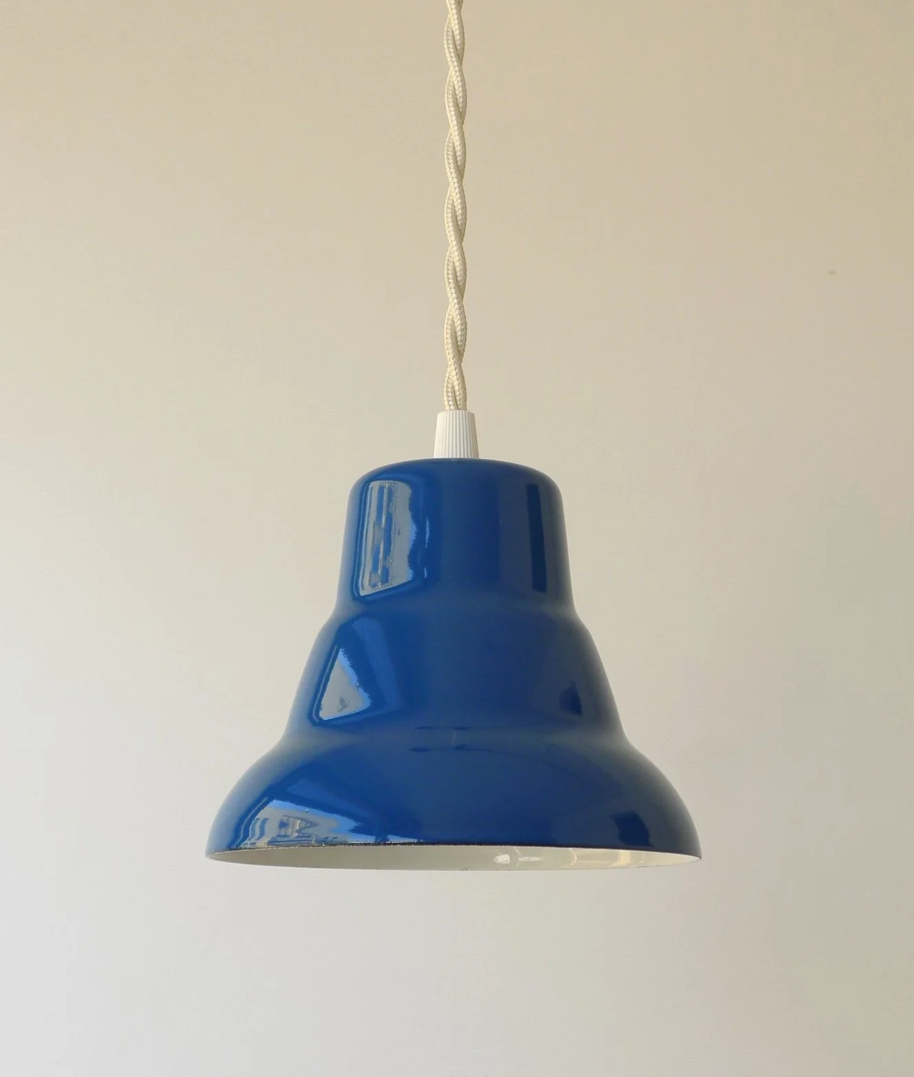 A blue pendant light fixture hanging from a white braided cord against a plain white wall.