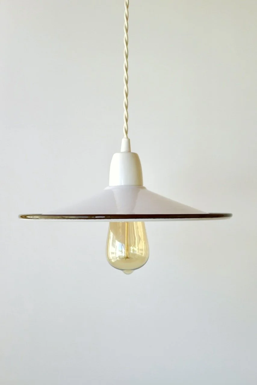 A modern white pendant light with a conical shade and an exposed filament bulb, hanging from a twisted white cord on a plain white wall background.