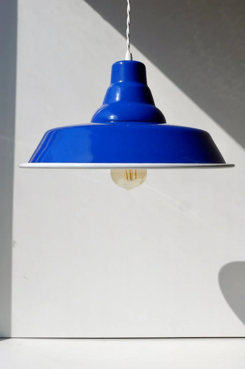 Blue pendant lamp hanging from a twisted cord against a white wall.
