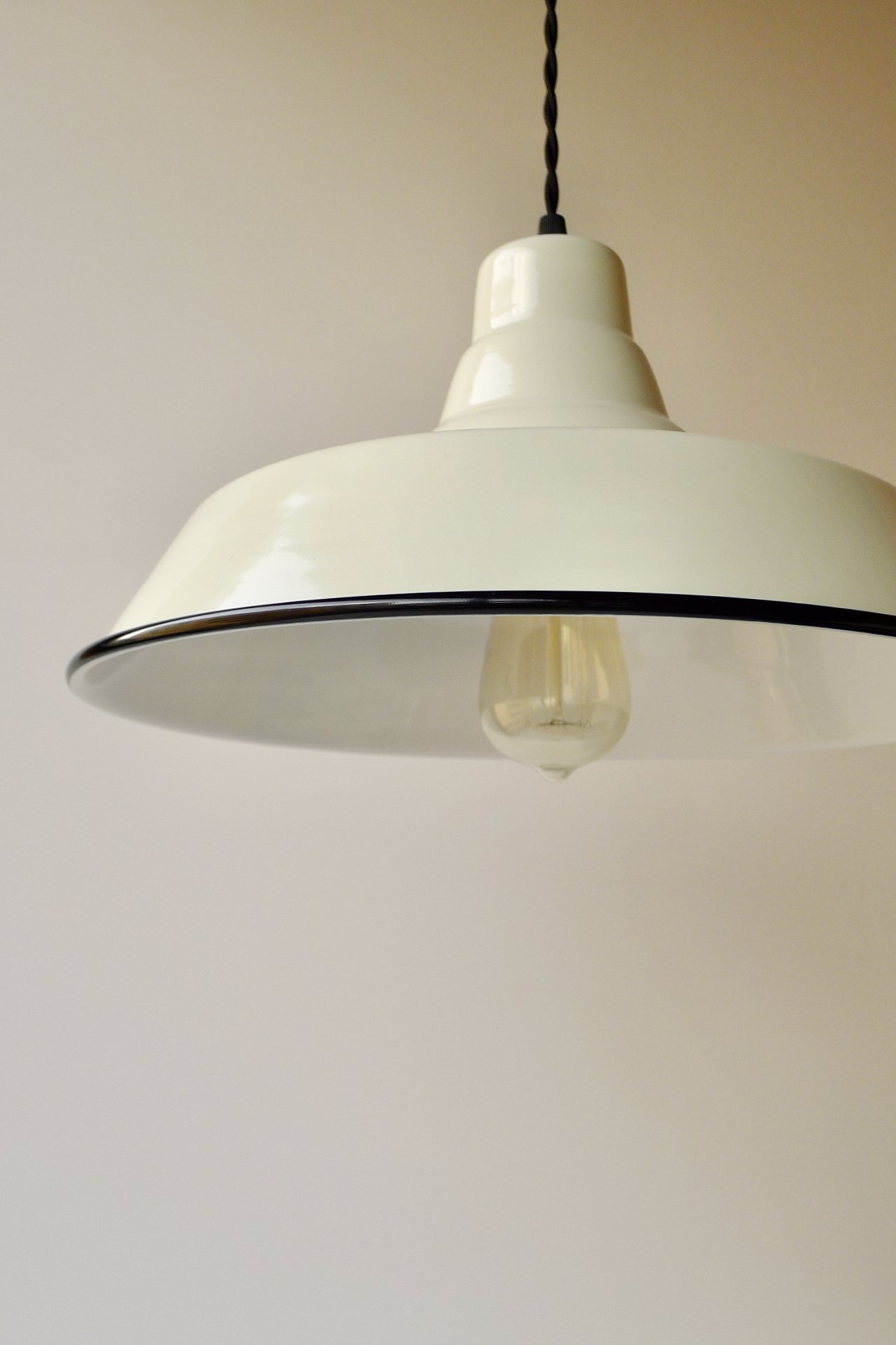 Light-cream ceiling pendant light with a black twisted cord hanging from a plain white ceiling.