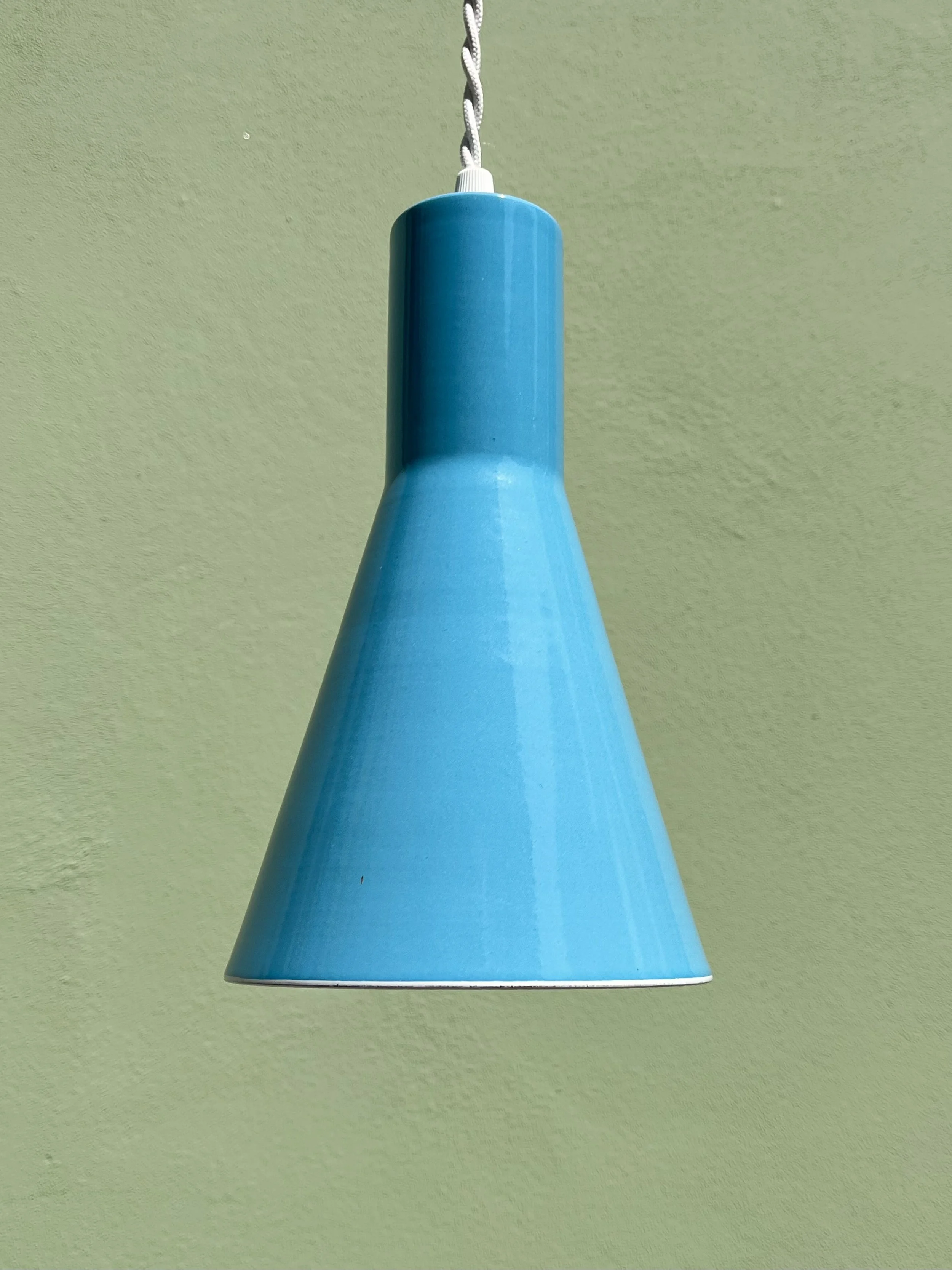 Blue cone-shaped lamp hanging from a white twisted cord against a green wall.