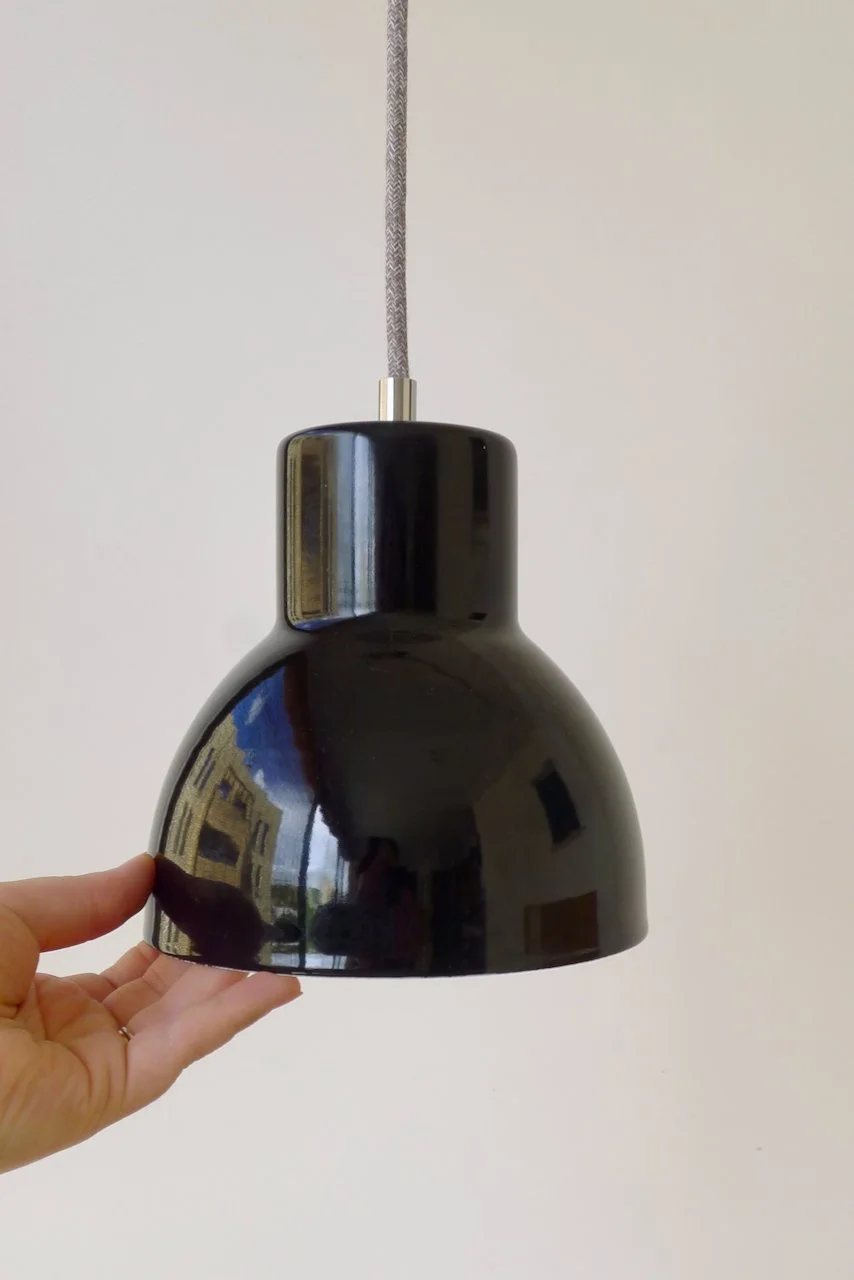 Black pendant light fixture hanging from a ceiling with a white wall background