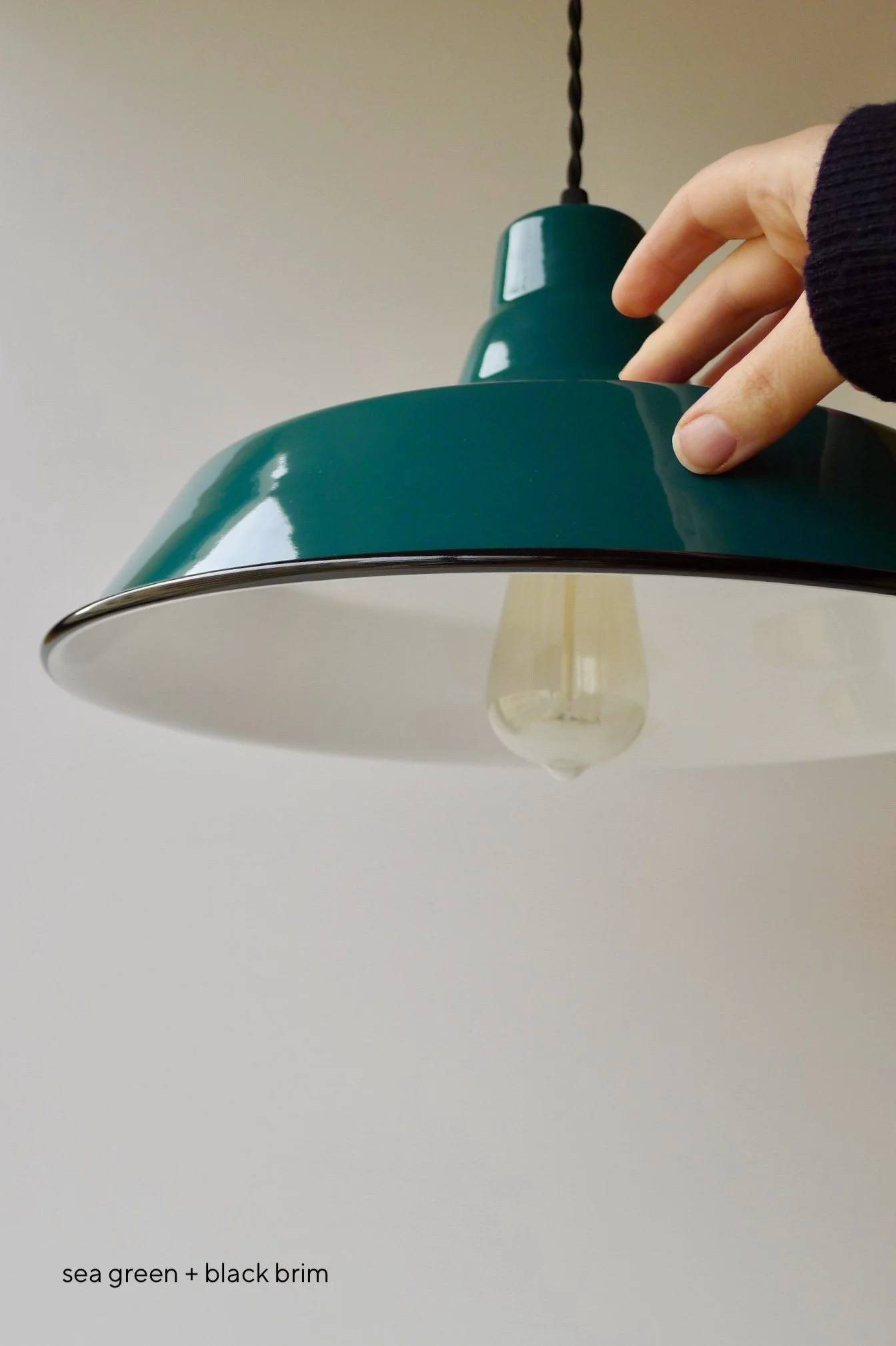 Sea green pendant light with a black brim and a white interior. The light fixture has a classic, industrial design with a visible Edison-style bulb. The text "sea green + black brim" is at the bottom.