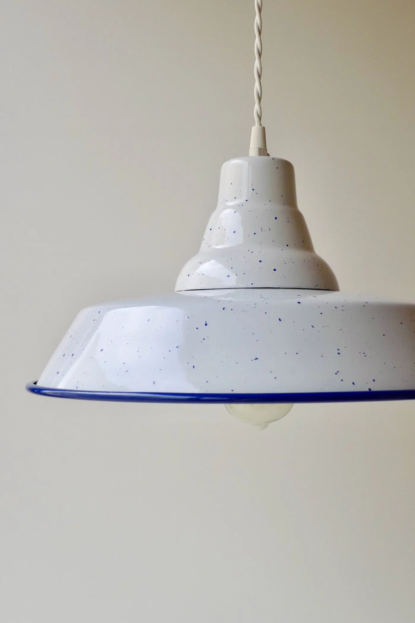 A white pendant light with a speckled pattern hanging from a twisted white cord against a plain, neutral-colored wall.