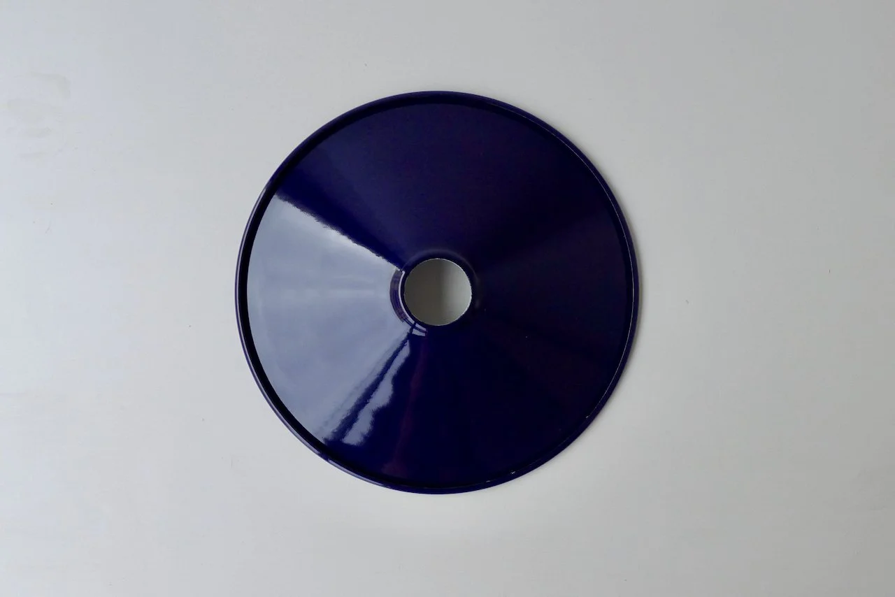 A dark blue round enamel shade resting on a white surface.