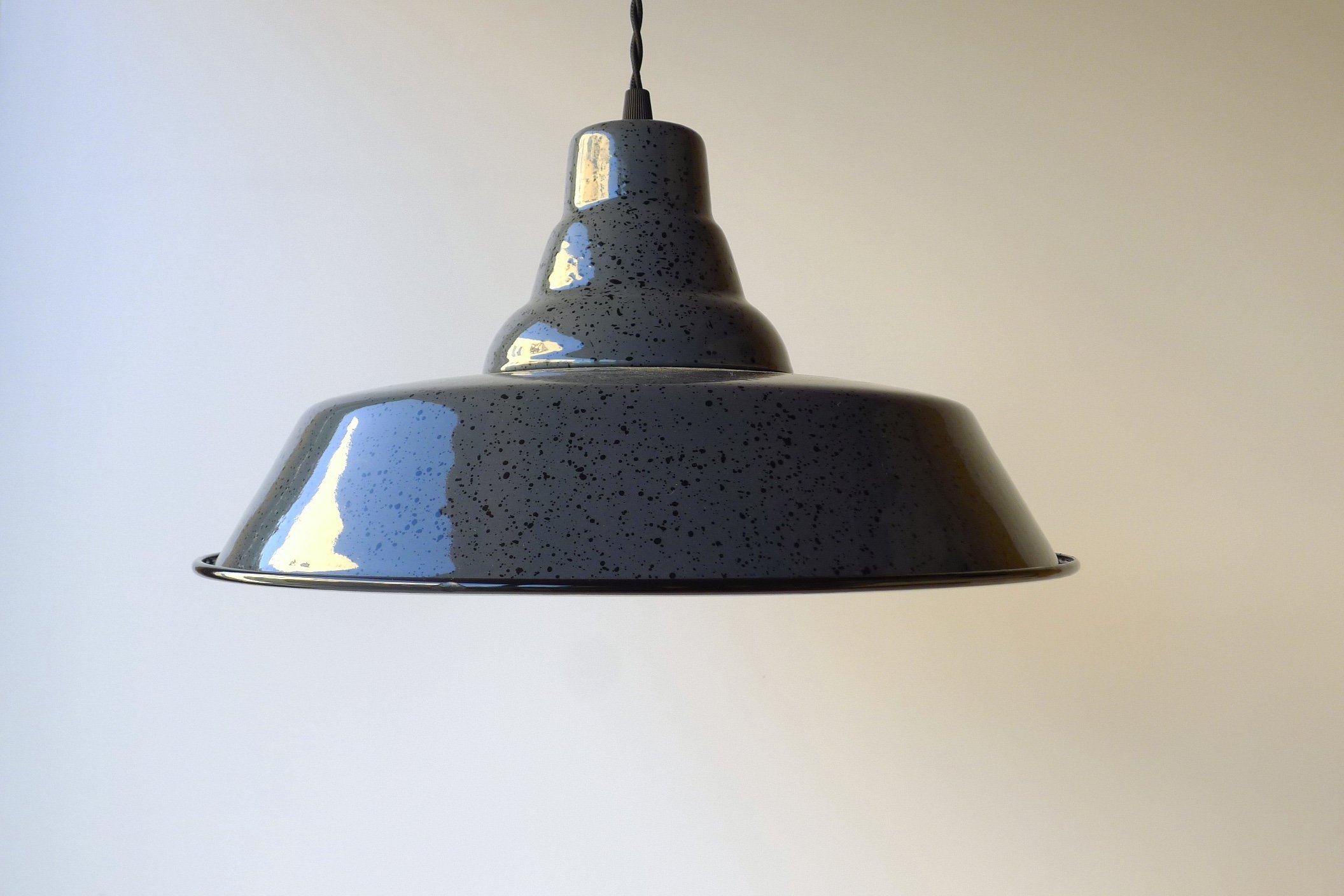 Close-up of a dark-grey pendant light with a speckled pattern hanging from the ceiling against a plain wall.