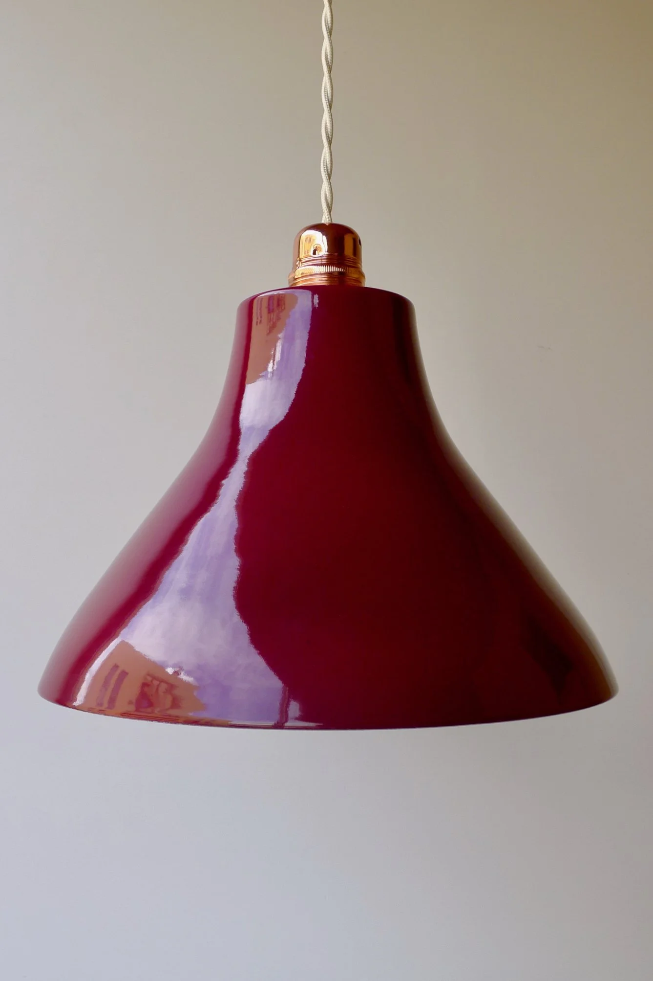 A close-up photograph of a burgundy hanging pendant lamp with a shiny surface, suspended by a twisted cord against a plain light background.