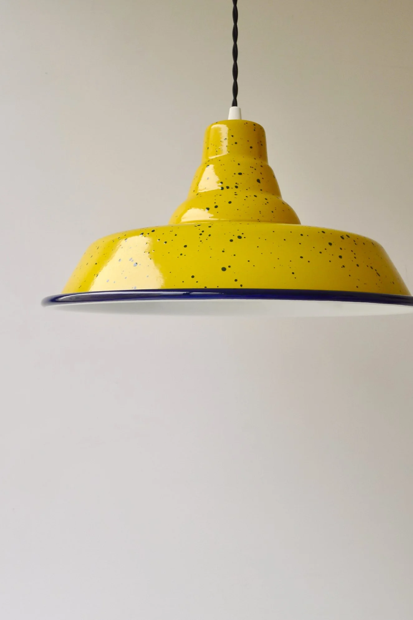 Yellow pendant light with dark-blue speckles hanging from a black twisted cord