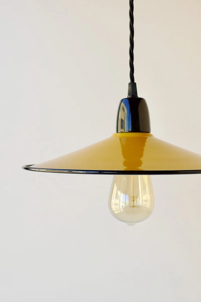 A hanging pendant light with a yellow shade and exposed light bulb against a plain white wall.