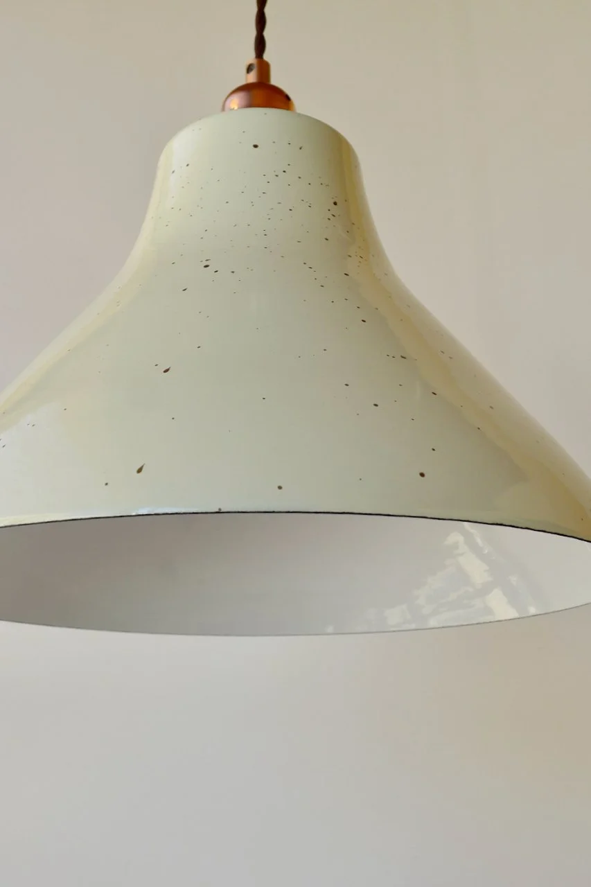 Close-up of a hanging white lampshade with small dark spots and a brown cord at the top.