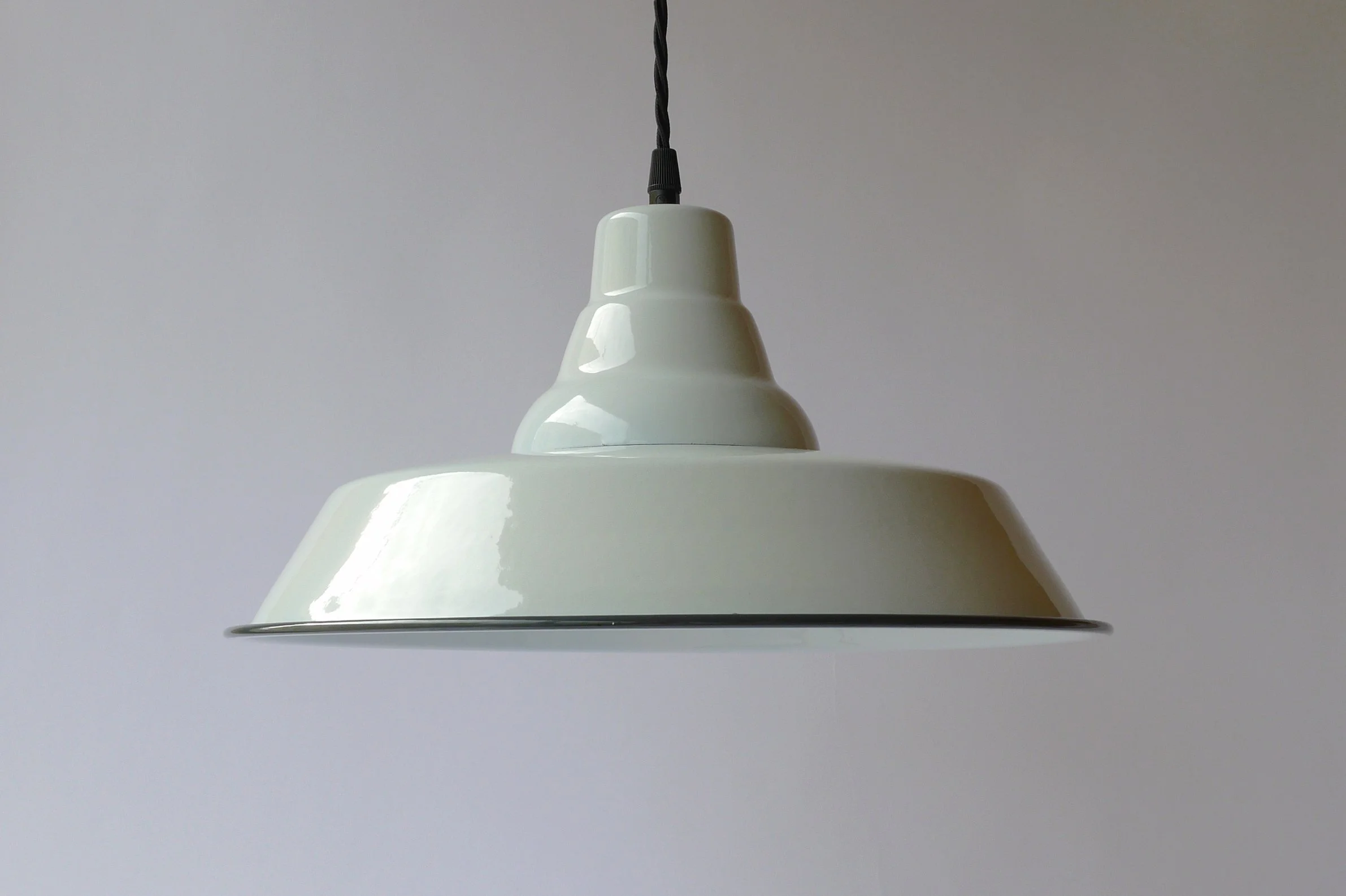 Close-up of a white pendant light hanging from a black cord against a plain light gray wall.