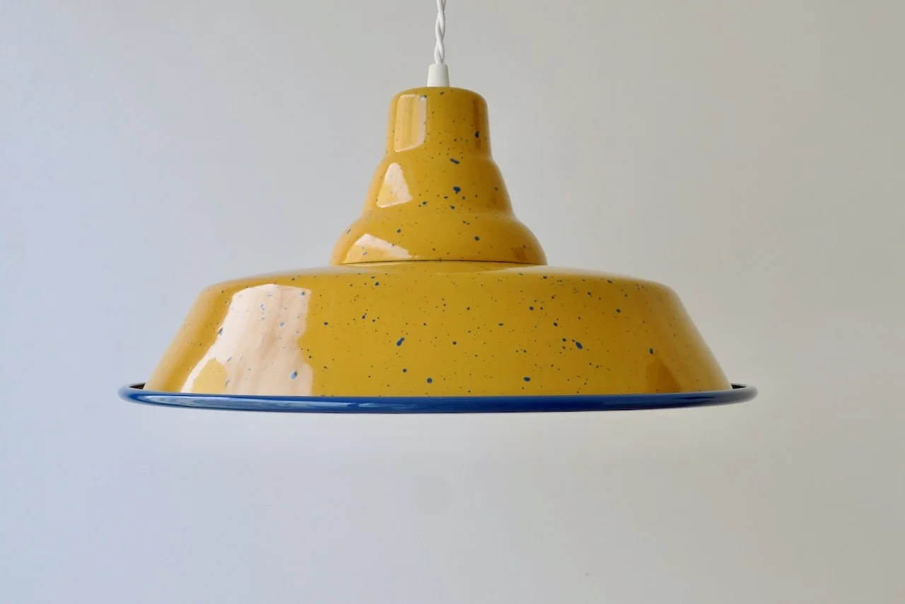 Yellow ceramic pendant light with speckled pattern hanging from a white cord against a white background.