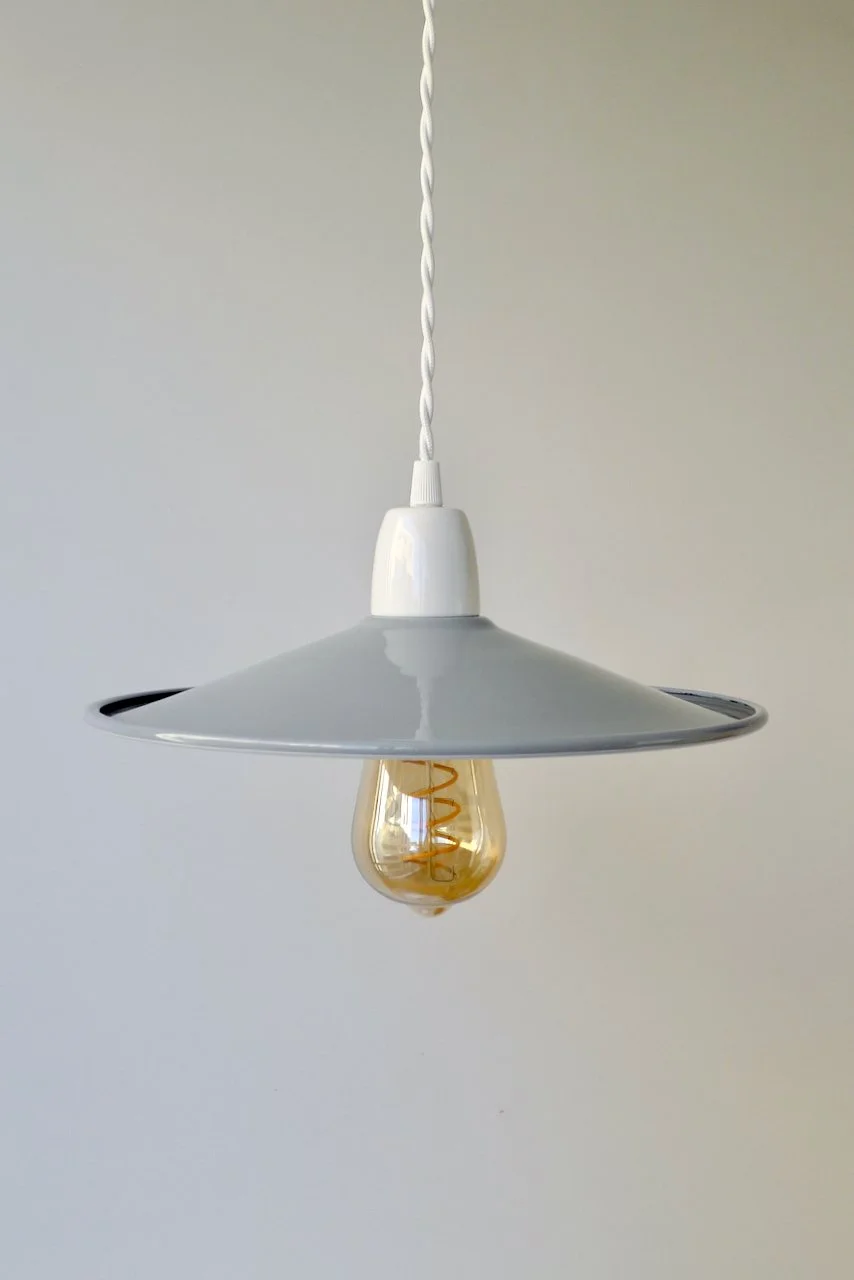 Modern light-grey pendant light with a visible Edison-style filament bulb, hanging from a twisted white cord against a plain light-colored wall.