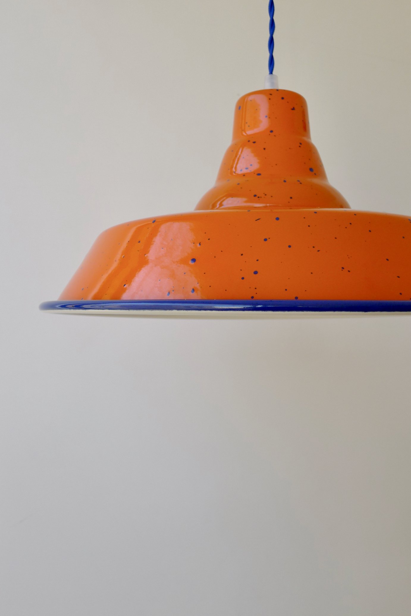 Close-up of an orange pendant light with blue speckles hanging from a twisted blue cord against a white ceiling.