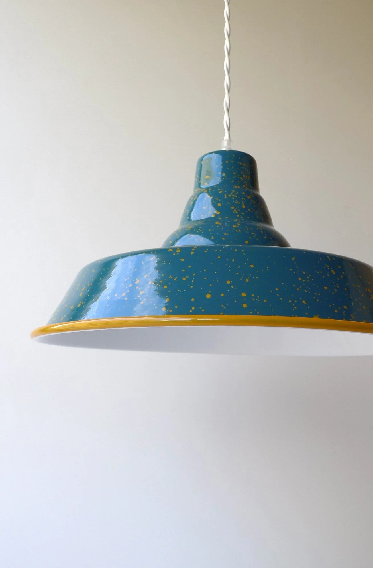 Blue pendant lamp with yellow speckles hanging from a white twisted cord against a plain white wall.