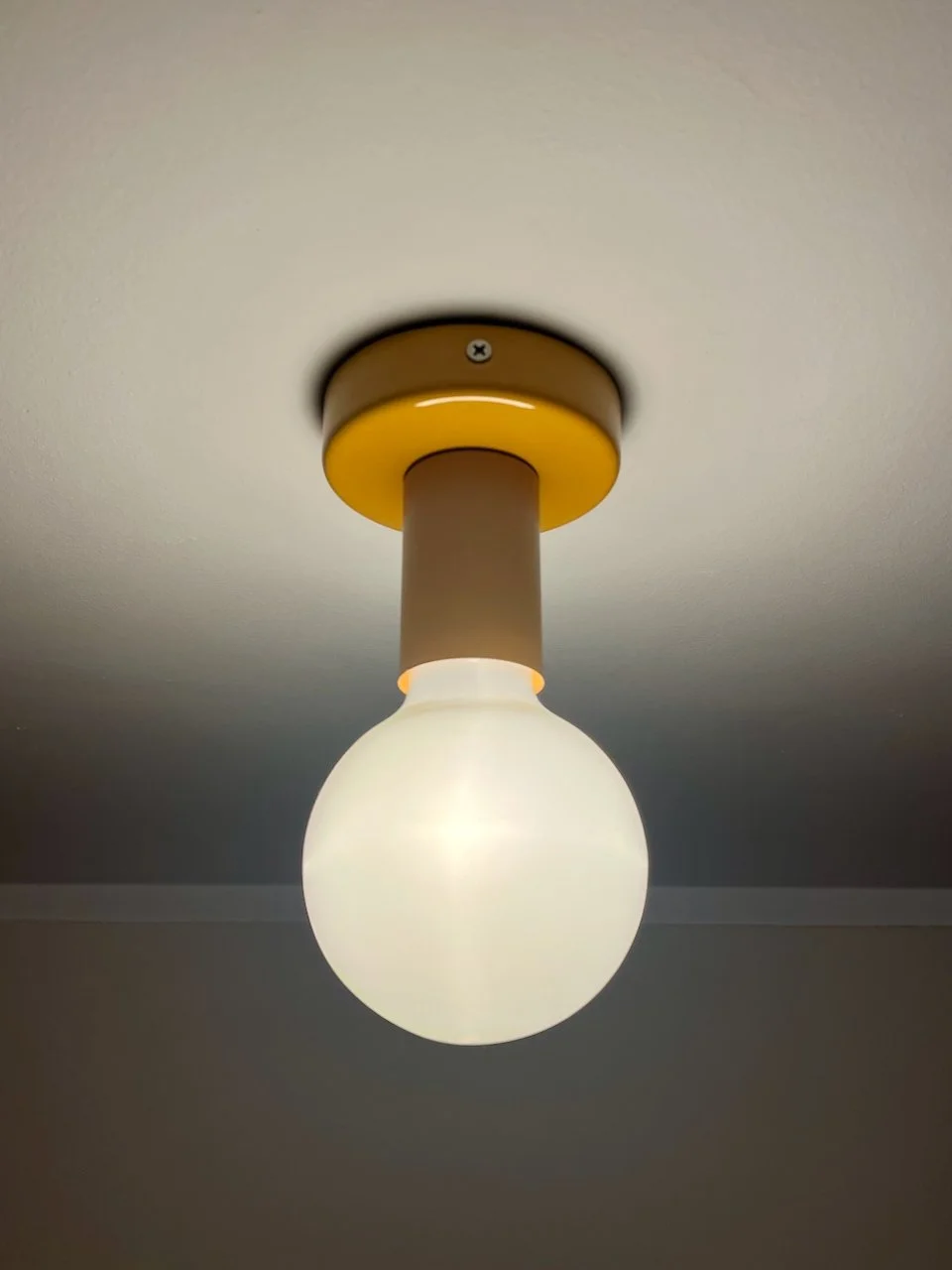 Ceiling light fixture with a frosted glass globe and a golden yellow base mounted on a white ceiling.
