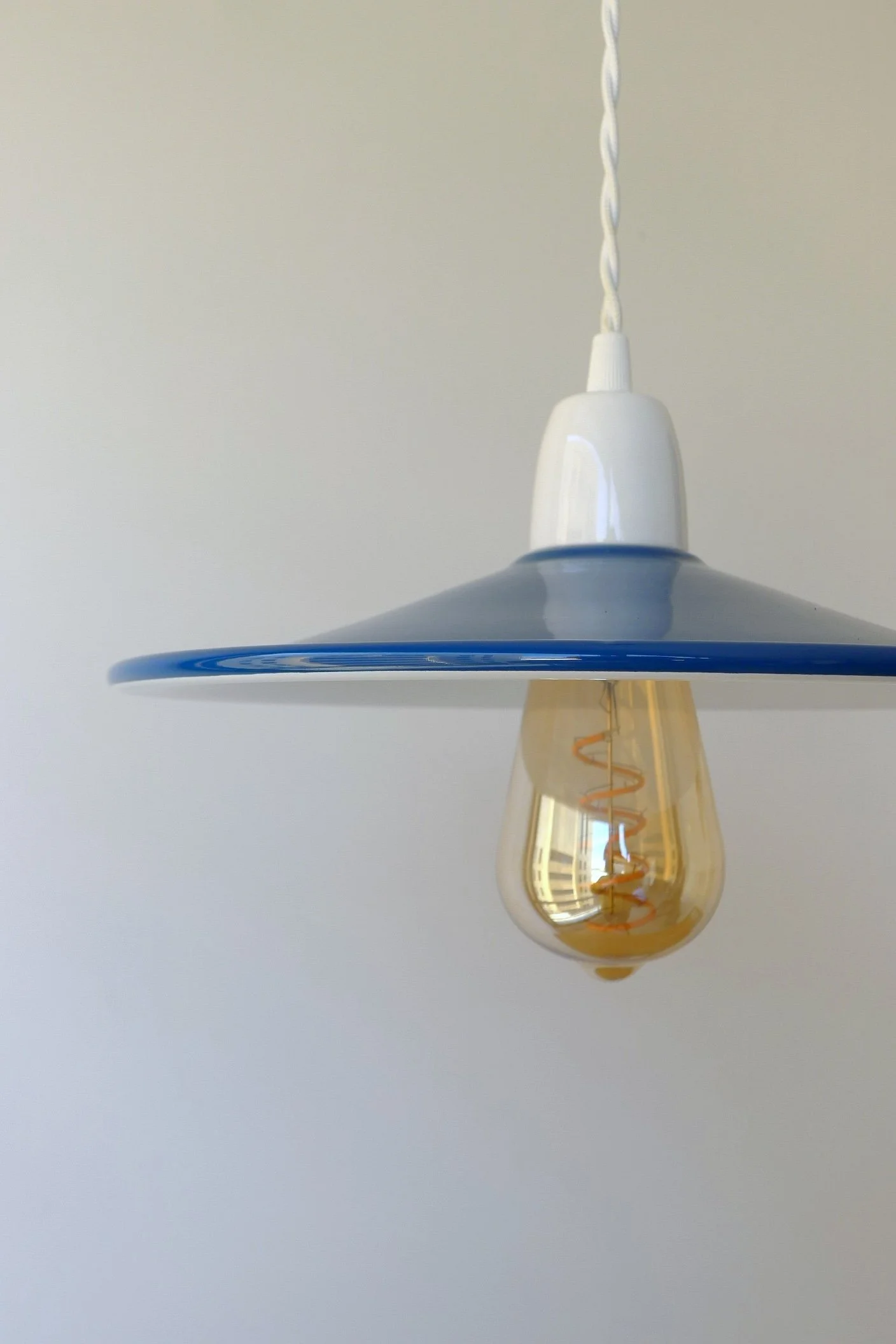 Close-up of a modern hanging lamp with a blue and white shade and an exposed filament light bulb hanging below it against a white wall.
