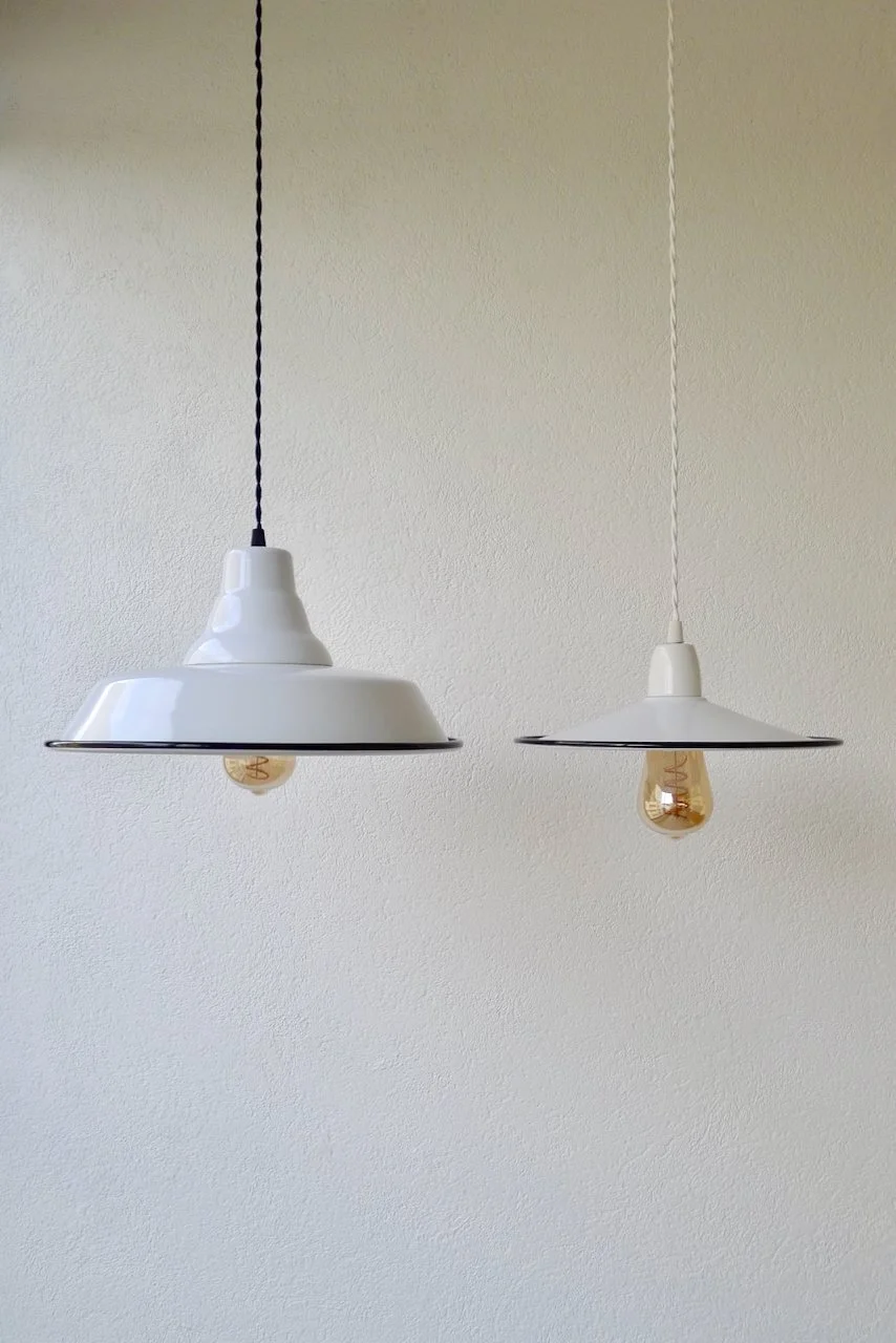Two hanging pendant lights with white shades and exposed filament light bulbs against a plain wall.