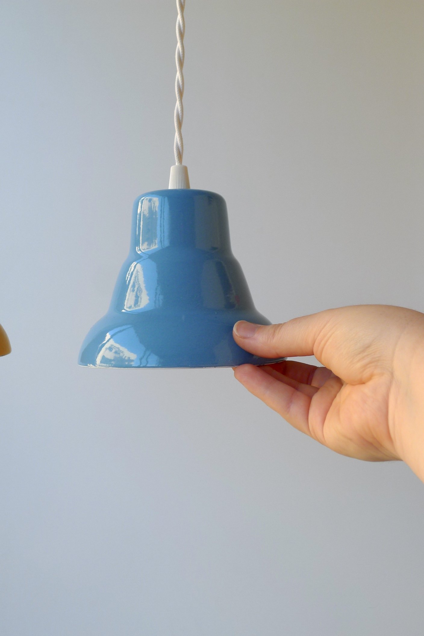 Small blue enamel lampshade against a light grey background, being held by a hand, for scale. The lamp is about the height of the palm of a hand.