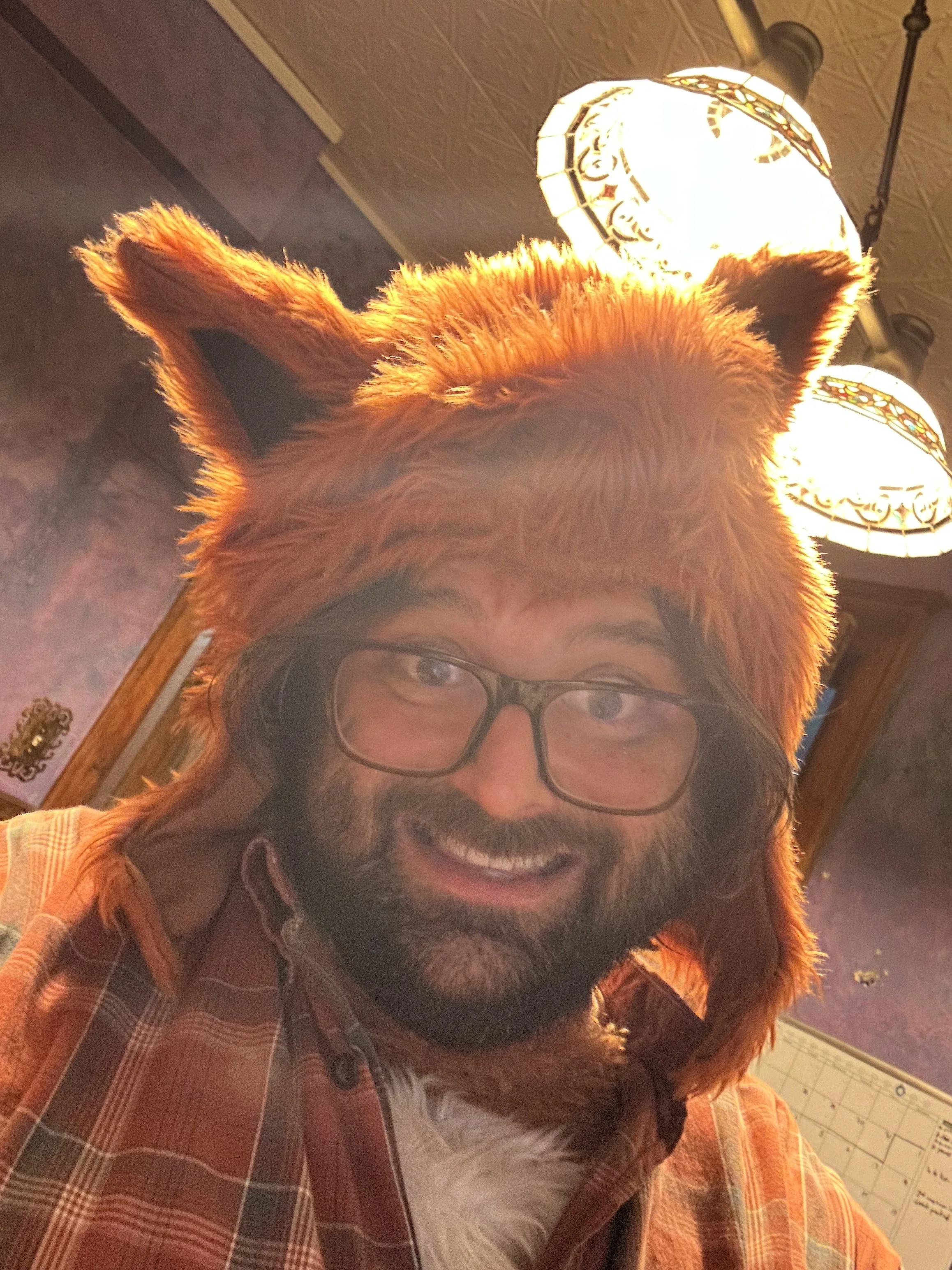 A man with glasses wearing a fox costume hat in a room with ornate ceiling lights.