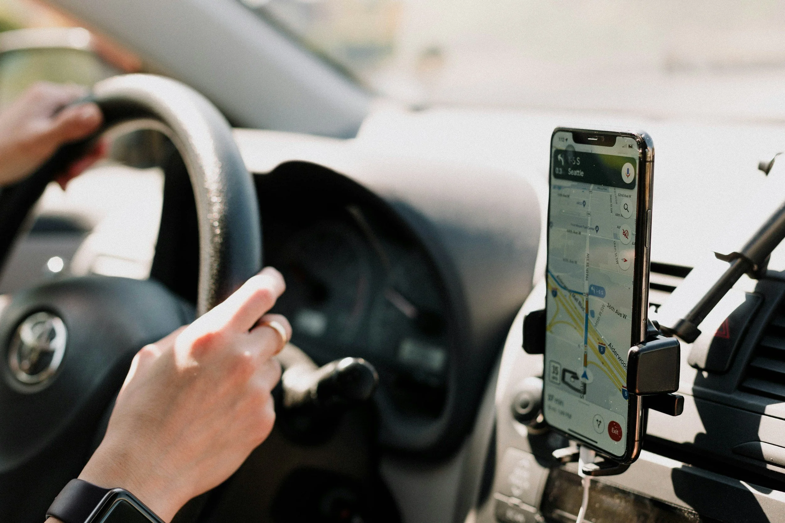 Person driving a car using a smartphone navigation app mounted on the dashboard.