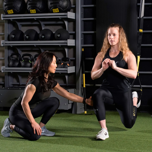 To kvinder træner i et fitnesscenter, en hjælper hjælper en anden med en øvelse.