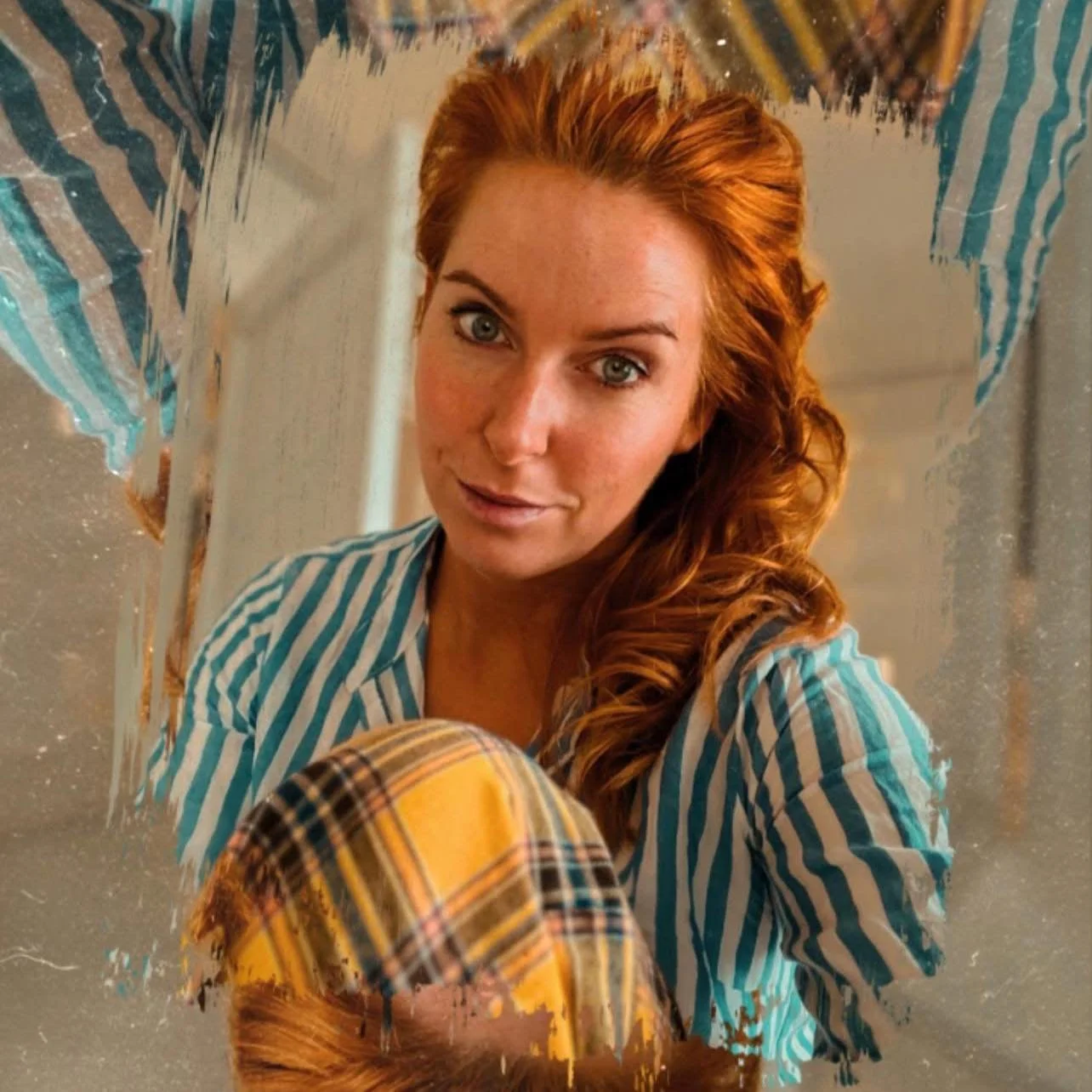 Et portræt af en rødklædt kvinde med blå øjne, iført en blå-hvid-stribet skjorte og gul-hvælvet bukser, taget i nærbillede med refleksion i en spejl.