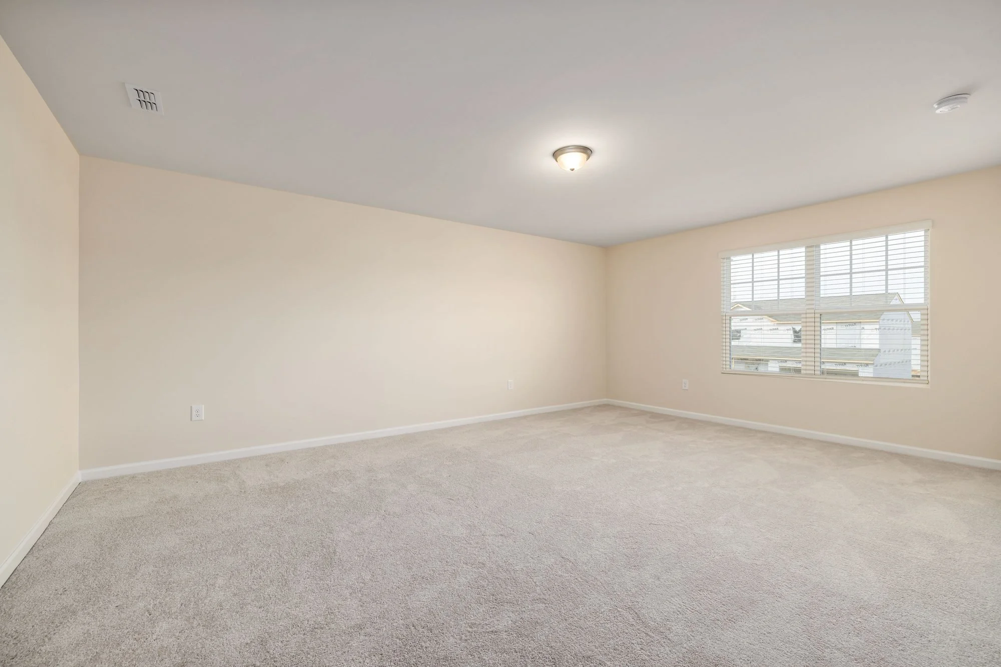 A wide corner view of an empty carpeted bedroom with beige walls and window blinds, the kind of shot to take during a move-in inspection.
