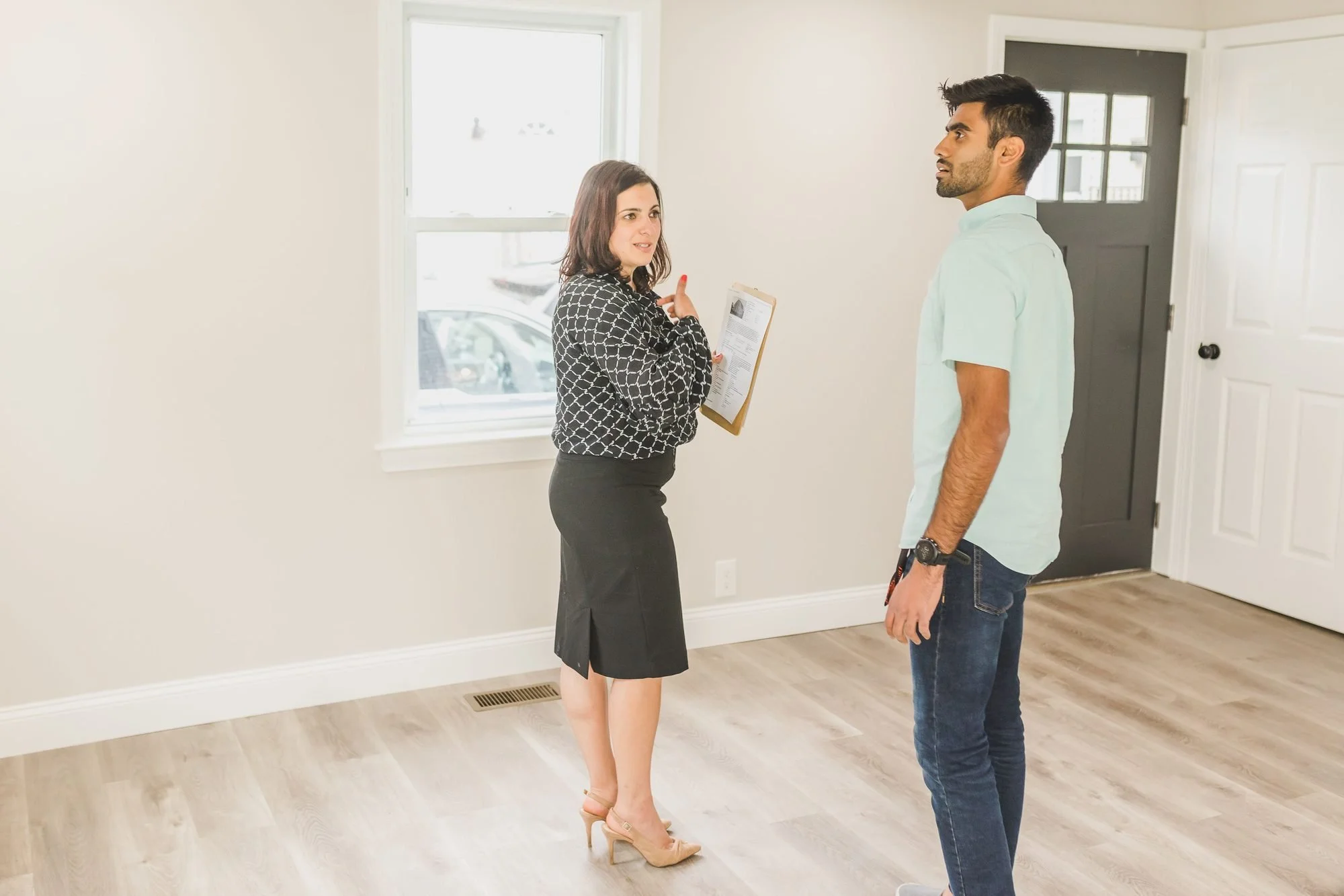 A property manager holding a clipboard walks a new tenant through an empty home with light wood floors before move-in.