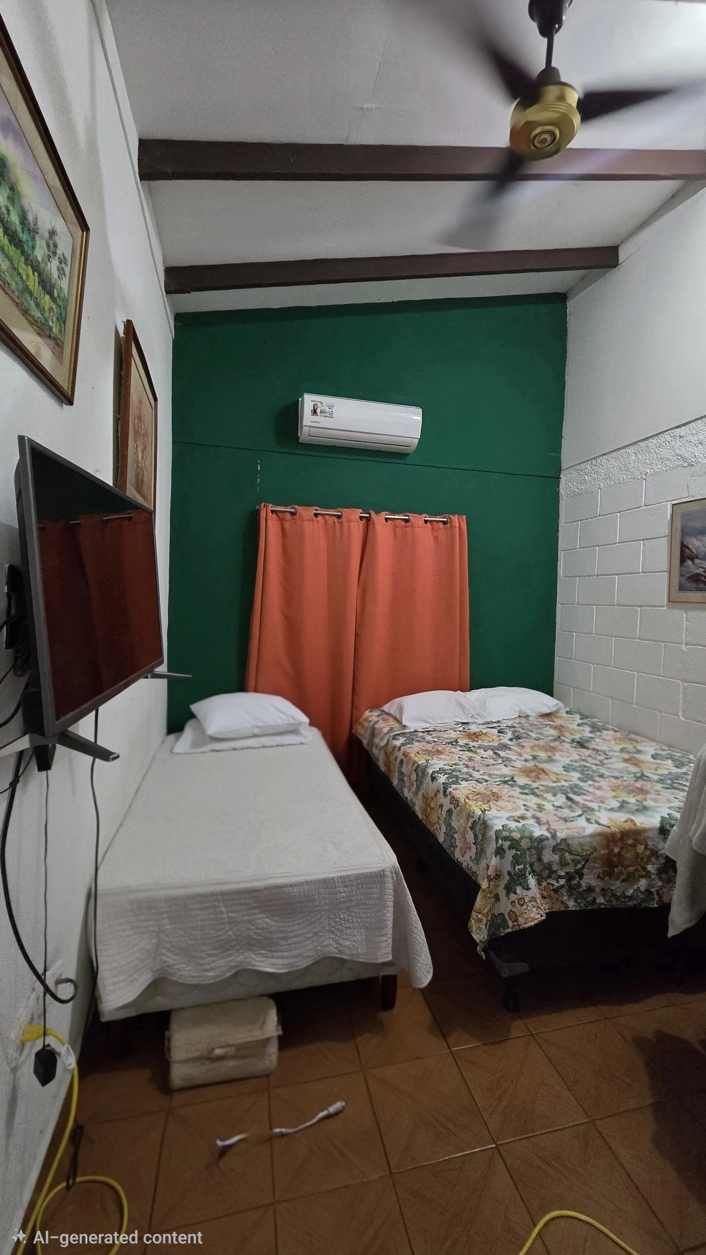 A small bedroom with two beds, one with a white bedspread and the other with a floral bedspread. Orange curtains cover a window behind the beds, and a green wall is behind the window. A wall-mounted air conditioner is above the window. A TV is mounte