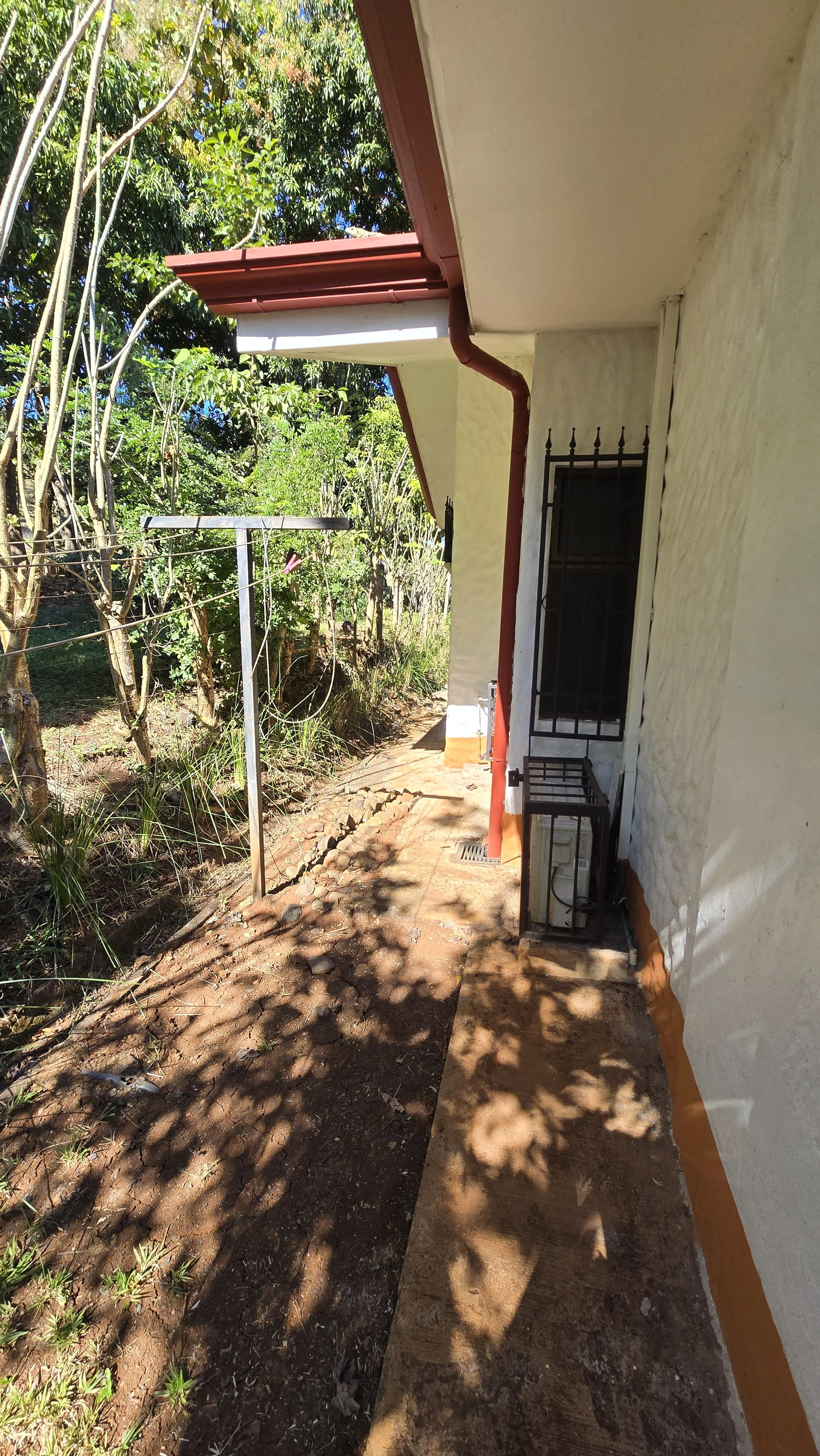 Side view of house exterior with a garden, clothesline, and shaded walkway.