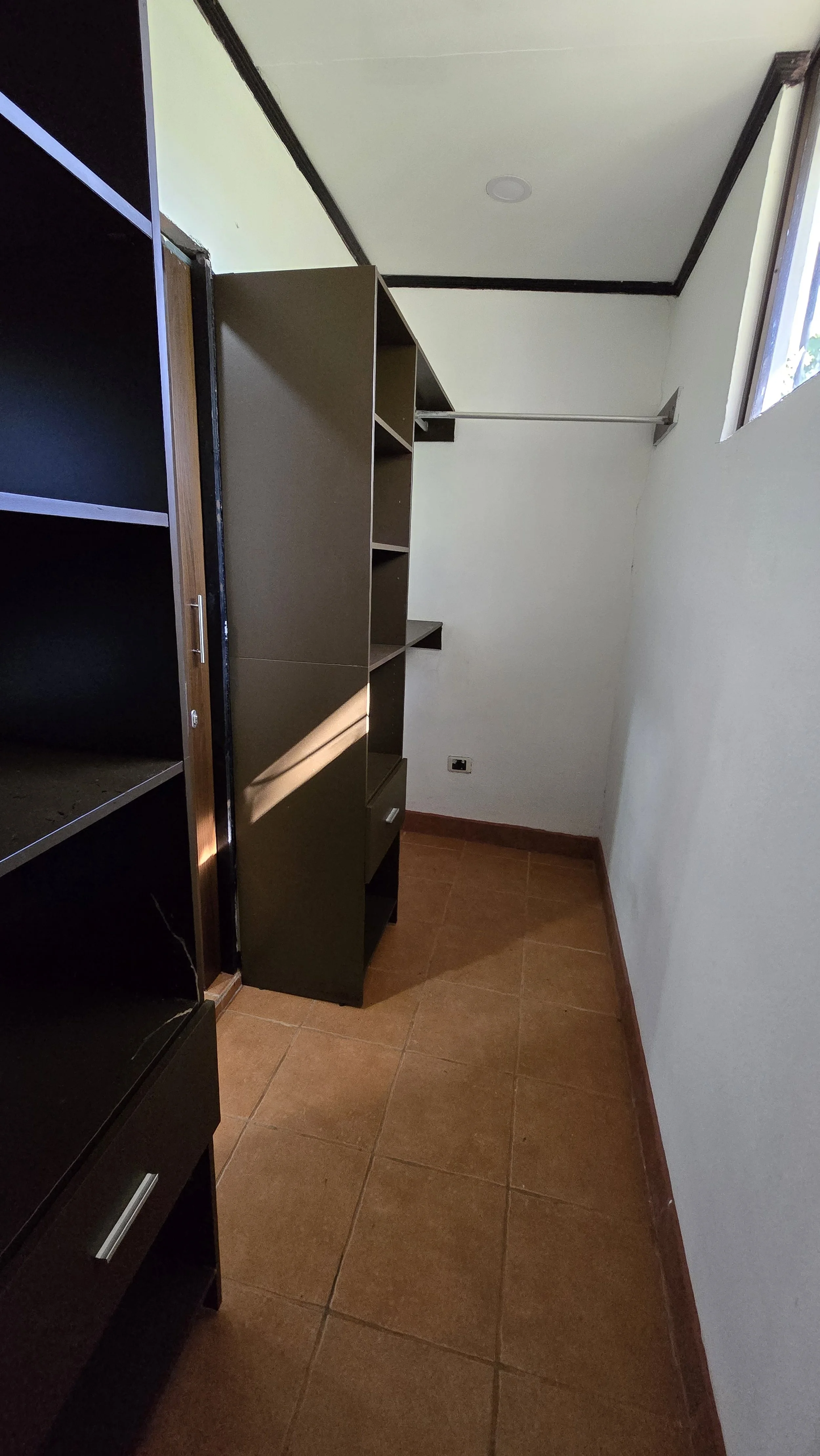 Empty closet with brown shelves, a white wall, and a small window.