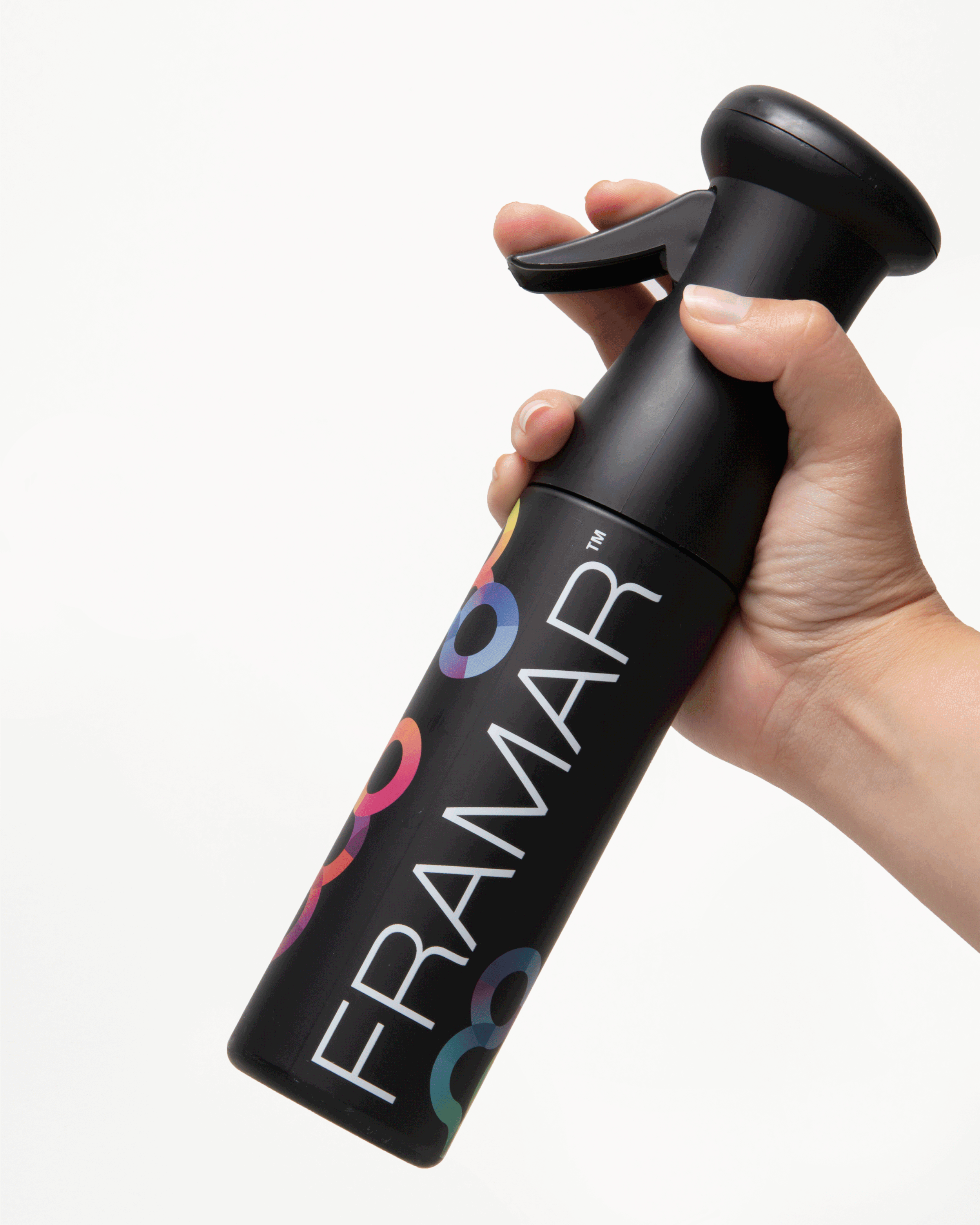 A hand holding a black Framar spray bottle with colorful circular graphics on a white background.