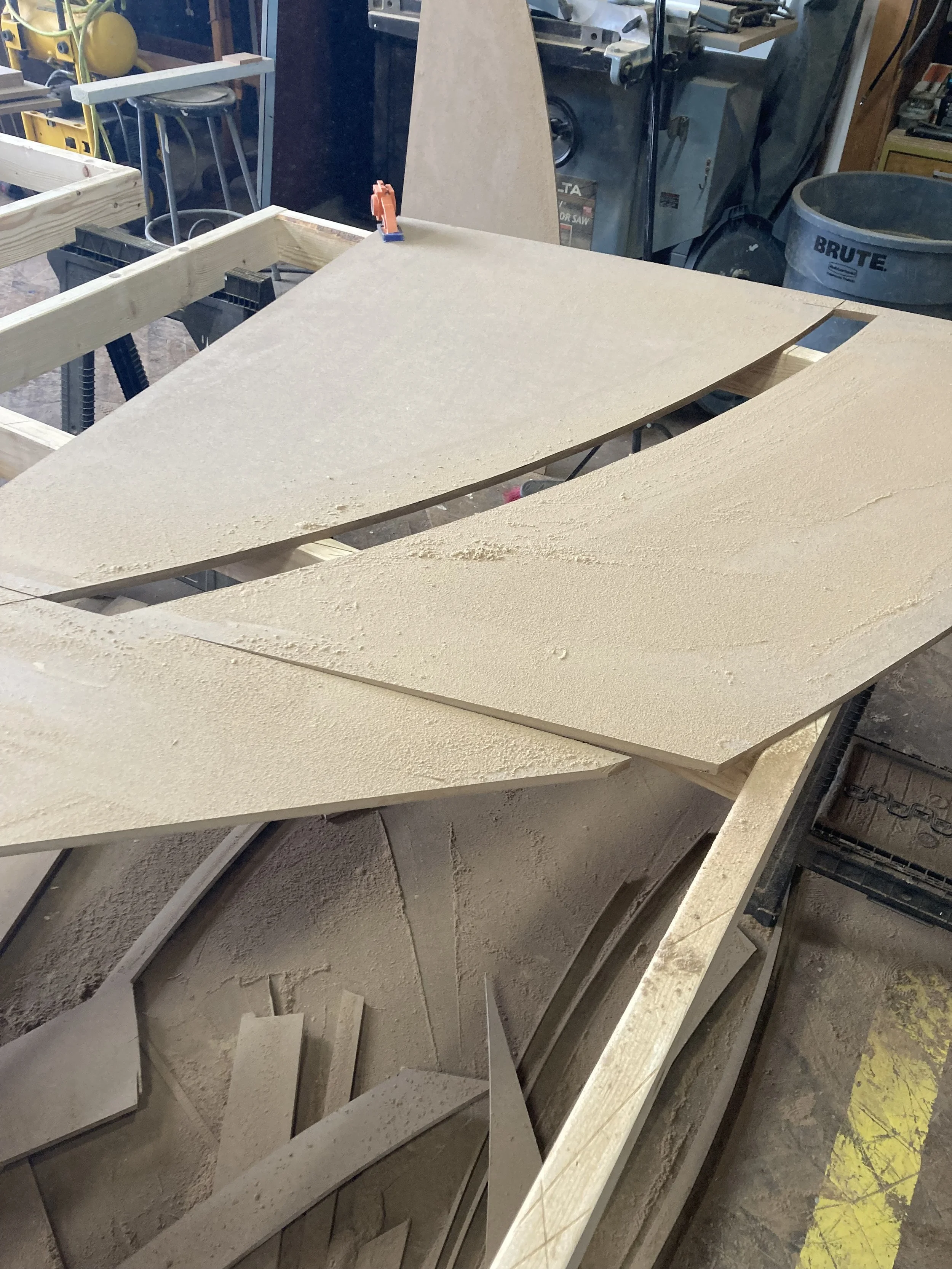 Sheets of cut plywood in a workshop with a small toy figure for scale.