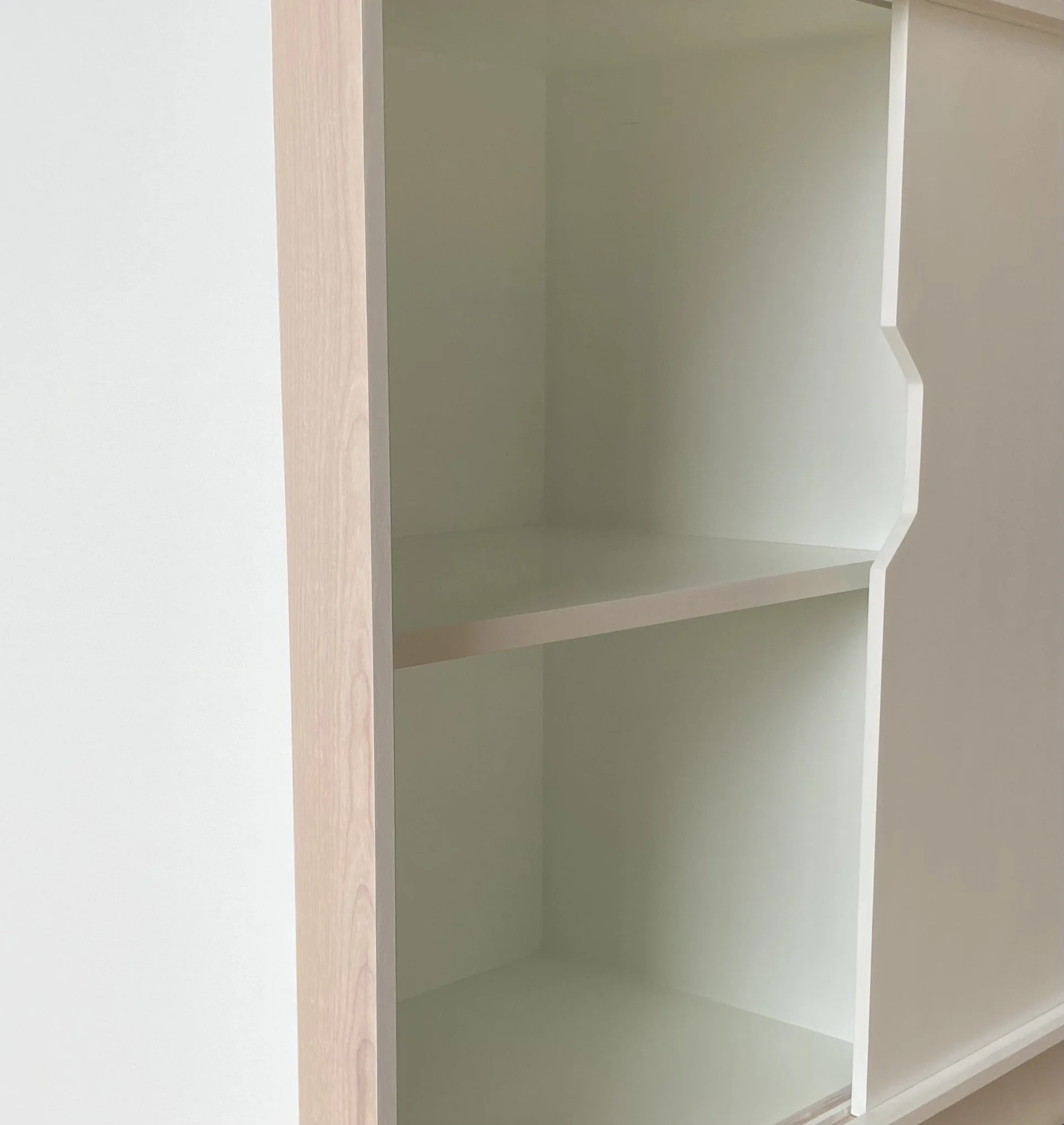Interior of an empty beige cabinet with two shelves and decorative cut-out on the edge.