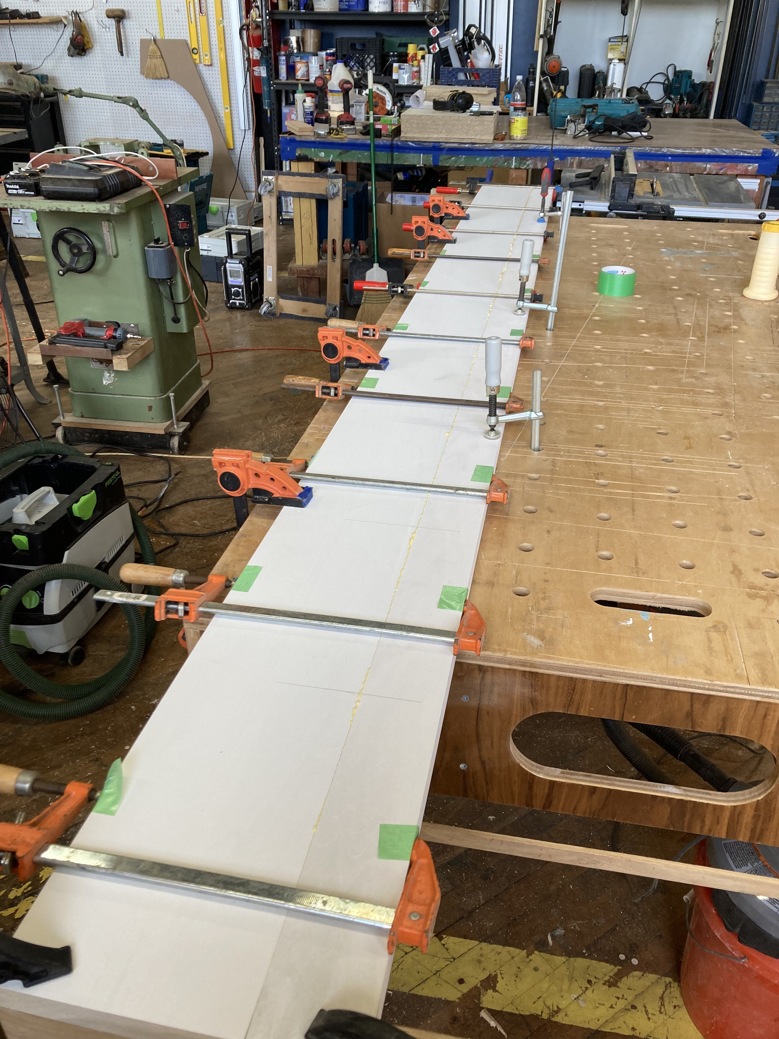 Woodworking shop with clamps holding a wooden board on a workbench