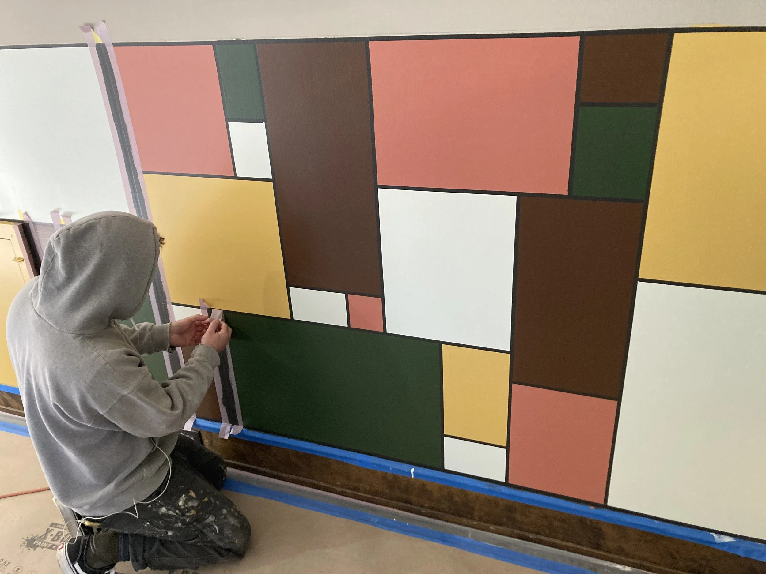 Person applying tape to a geometric mural with colorful rectangles.