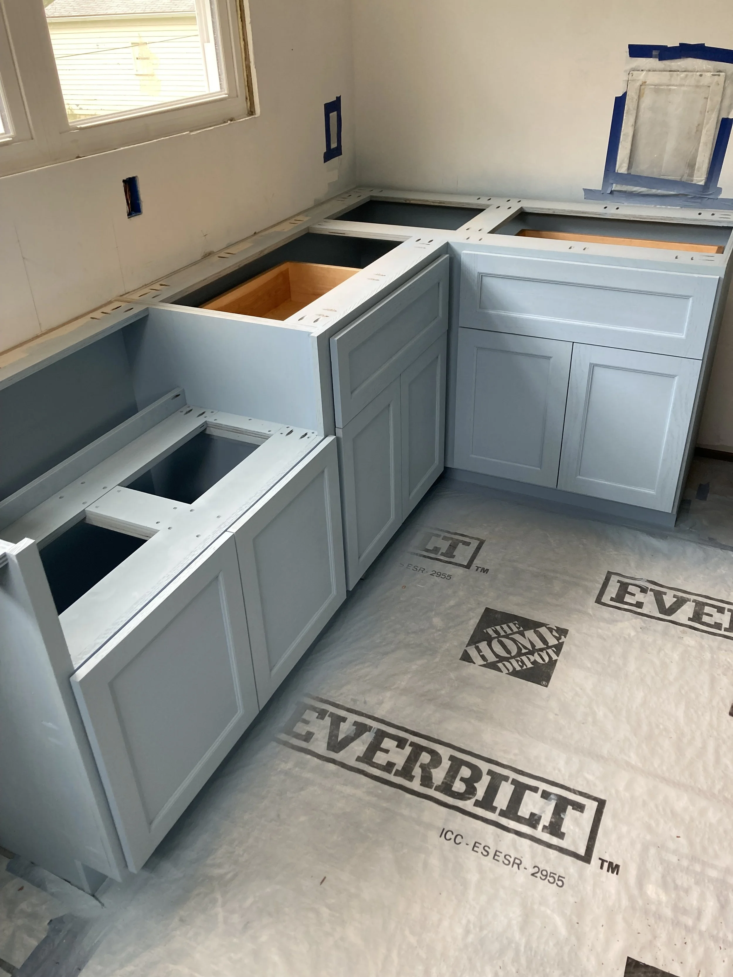 Partially installed light blue kitchen cabinets without countertops, protective floor covering branded Everbilt and Home Depot.