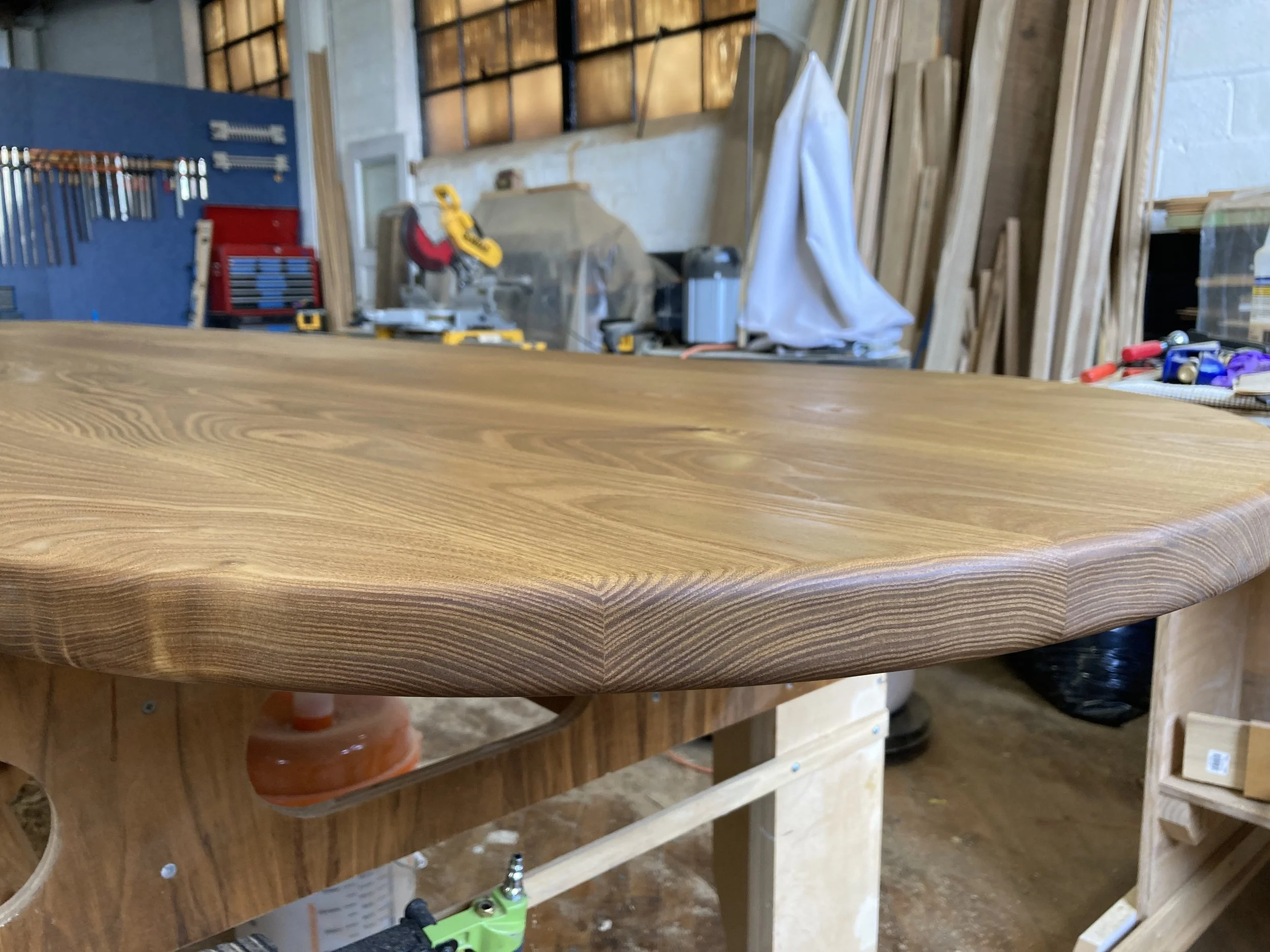 Wooden table surface in a workshop with tools and lumber in the background.