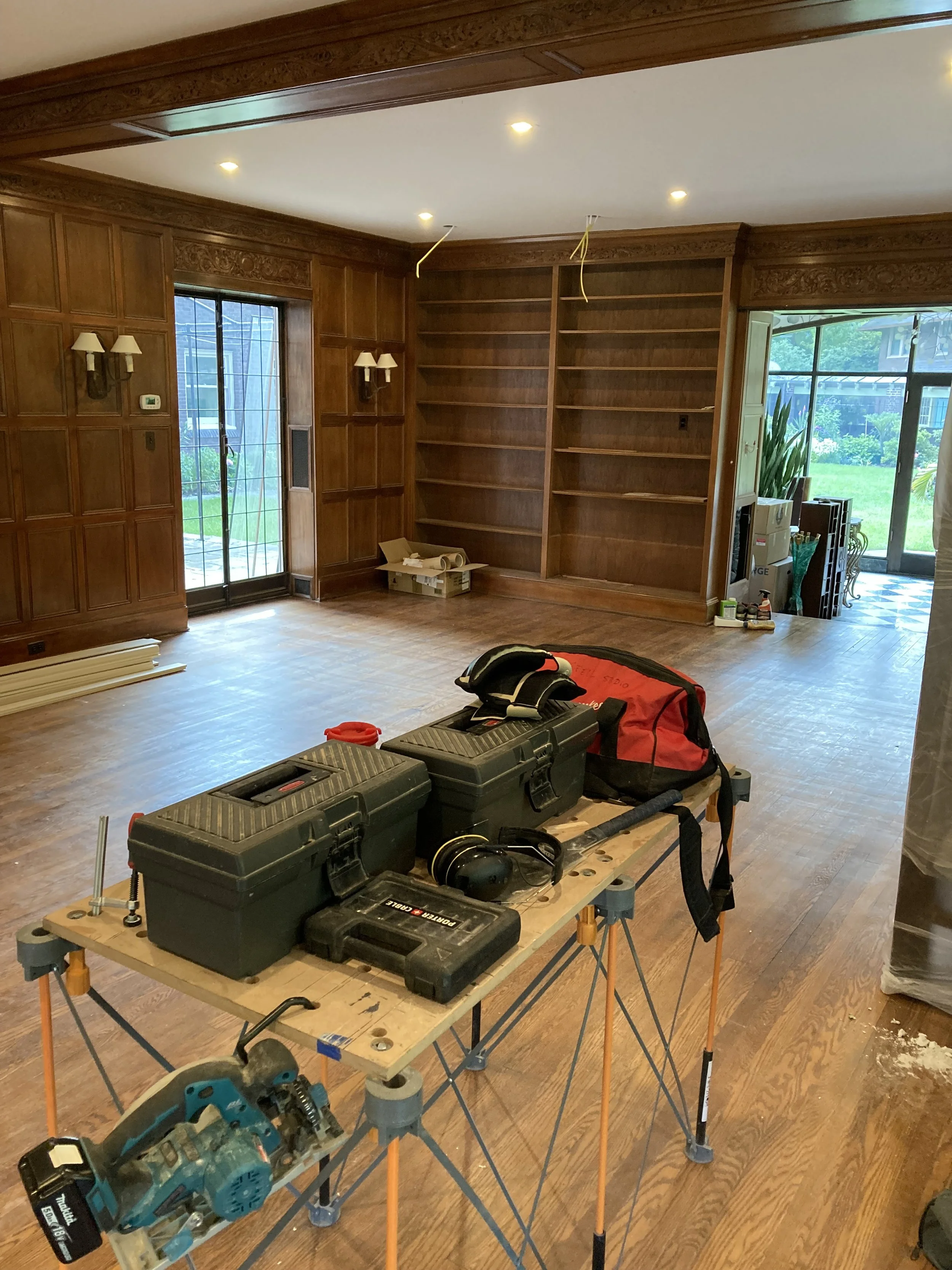 Room with wooden paneling, built-in bookshelves, a sliding glass door, and construction tools on a table.