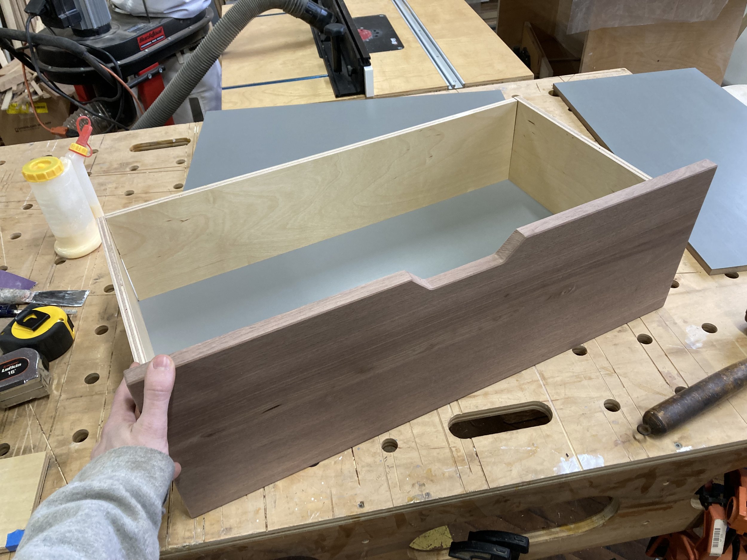 Person building a wooden drawer on a workbench with woodworking tools.