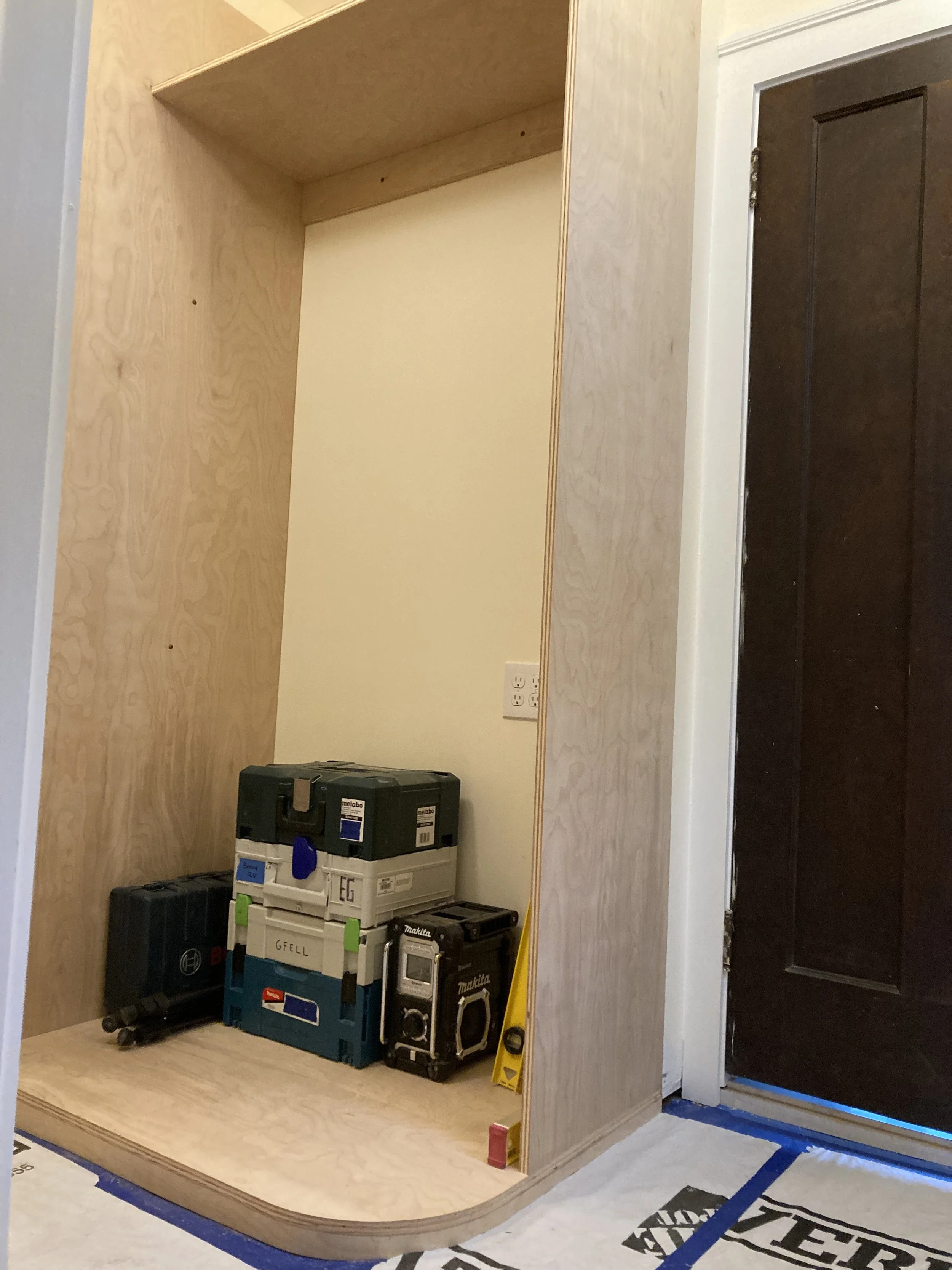 Wooden cabinet interior with stacked toolboxes and a Makita radio next to a yellow level and red block.