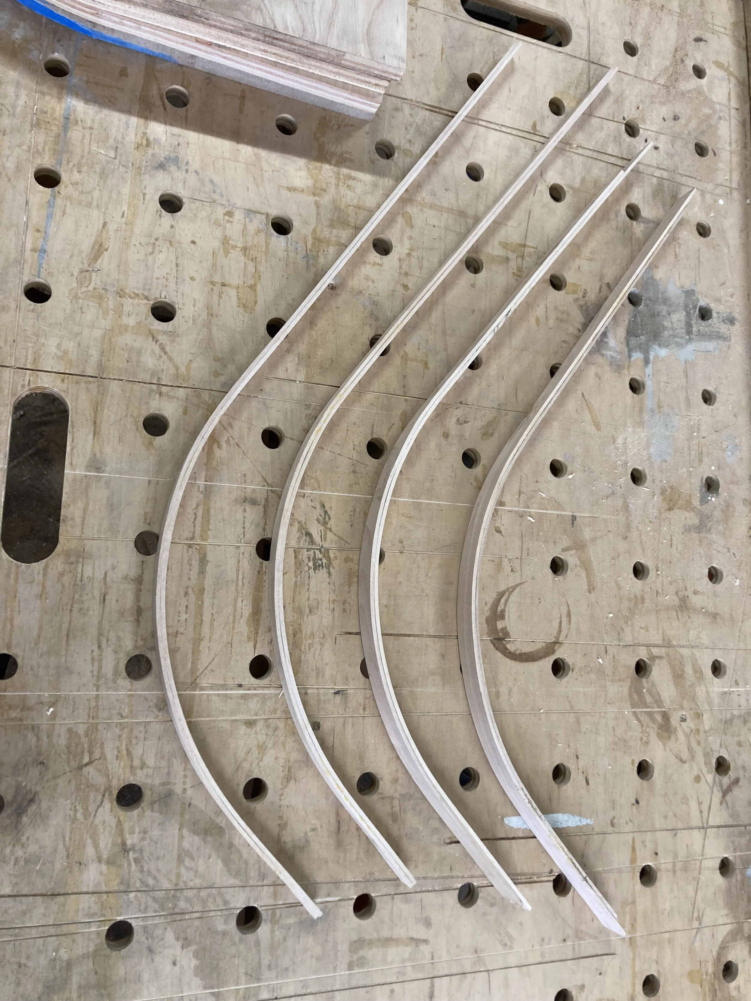 Curved wooden pieces placed on a perforated workbench surface.