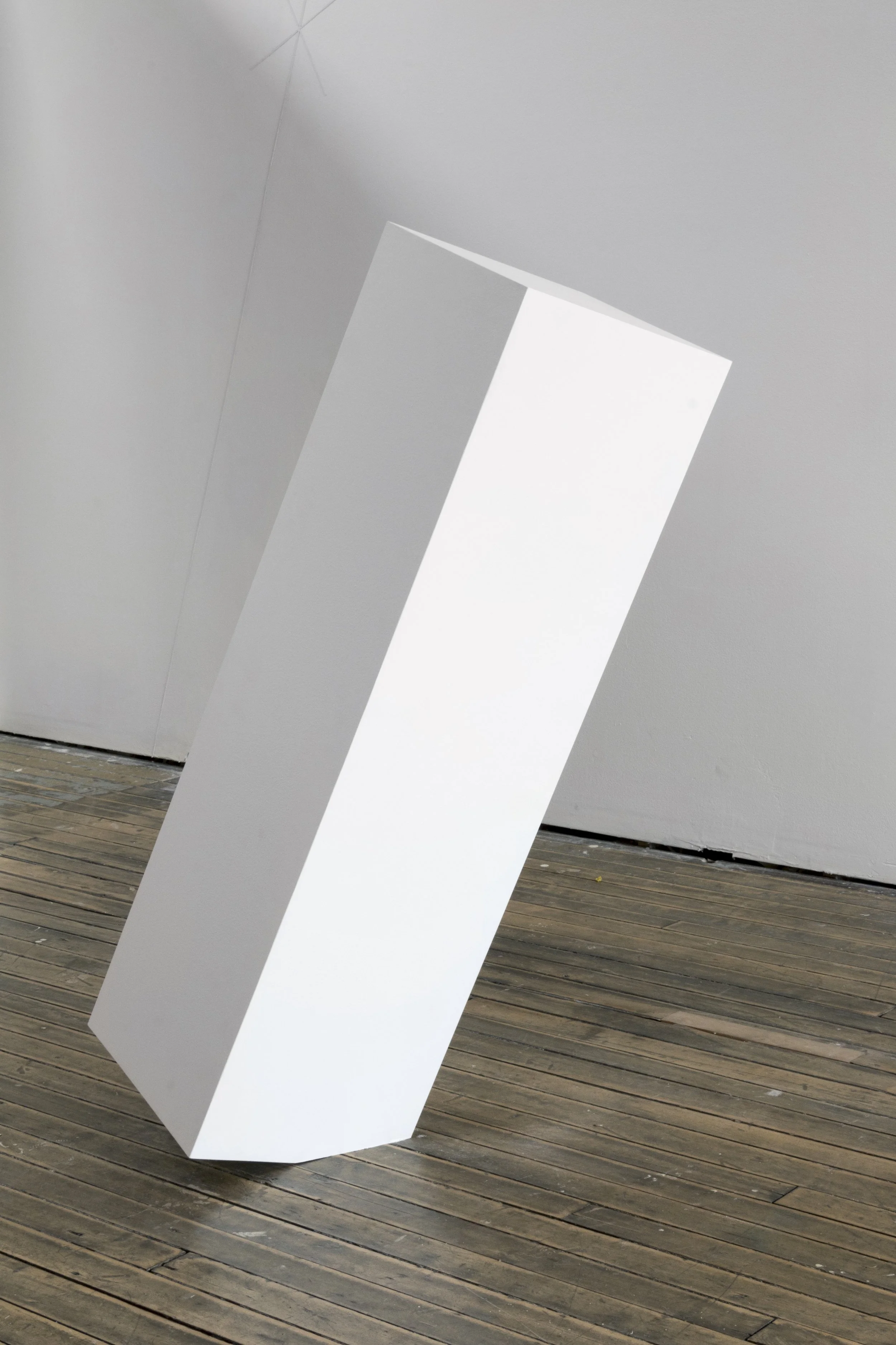 Leaning white rectangular sculpture on wooden floor
