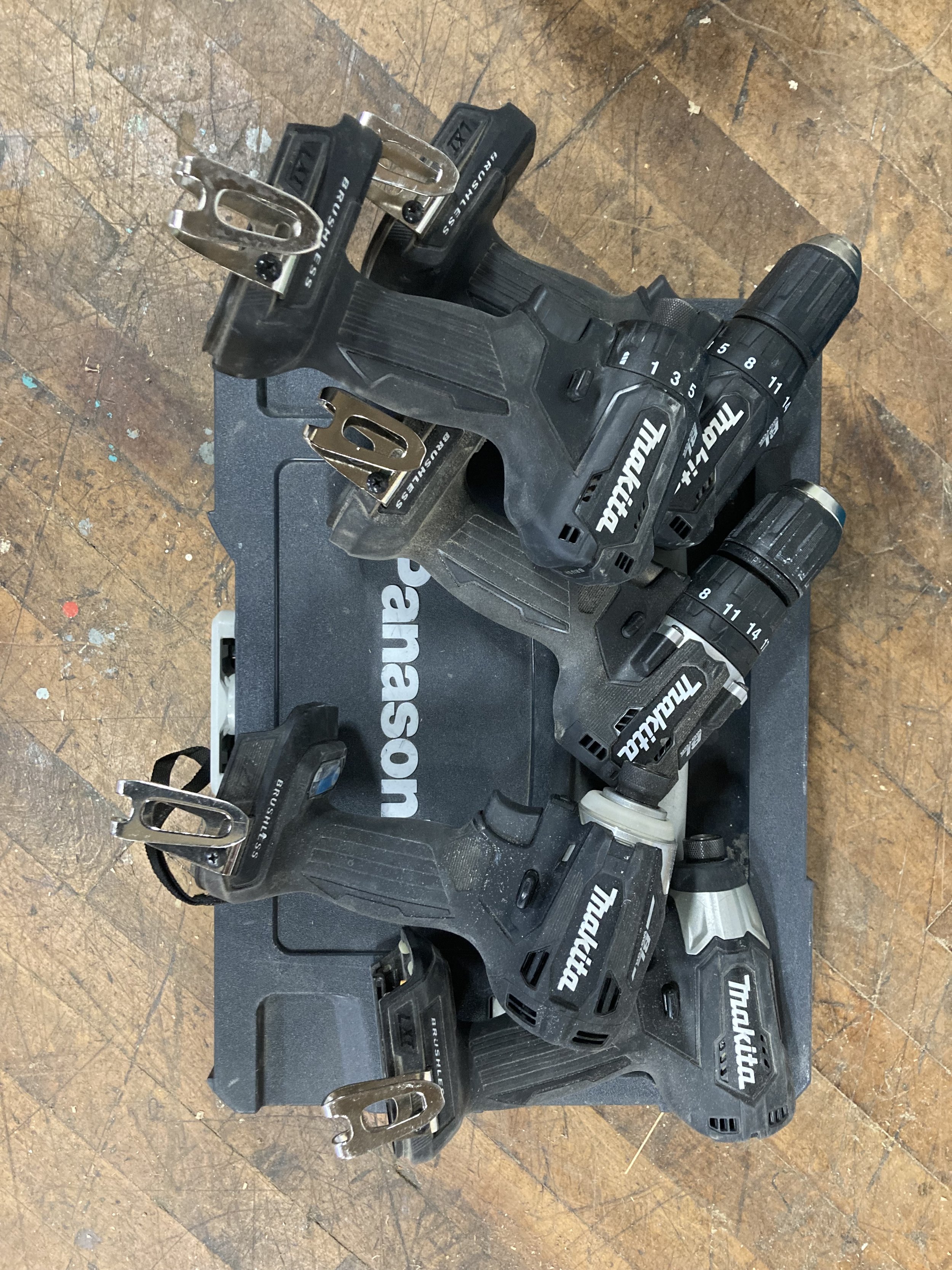 Cluster of Makita power drills on a Panasonic case, placed on a wooden surface.