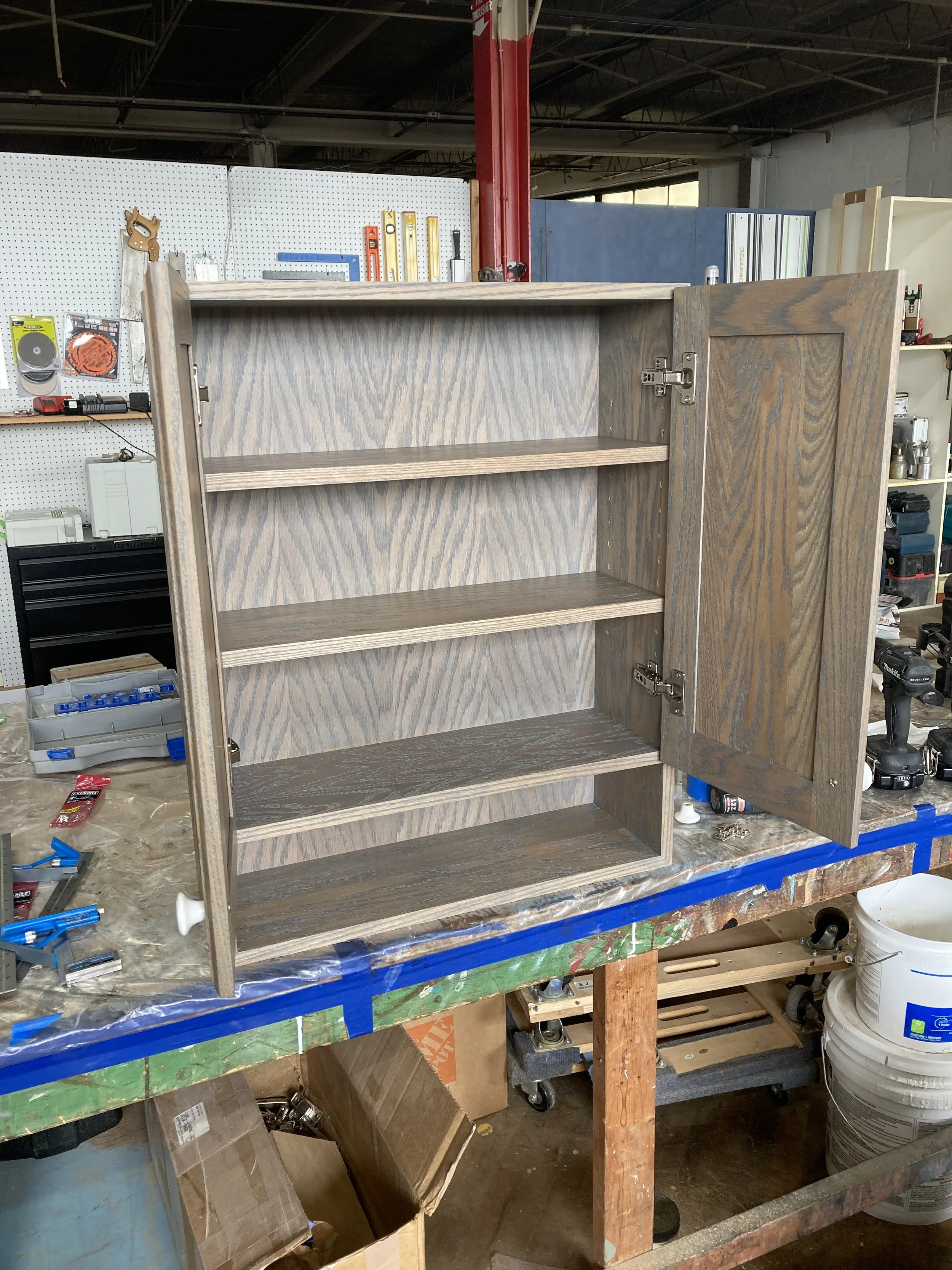 Wooden cabinet with open door and shelves in workshop setting.